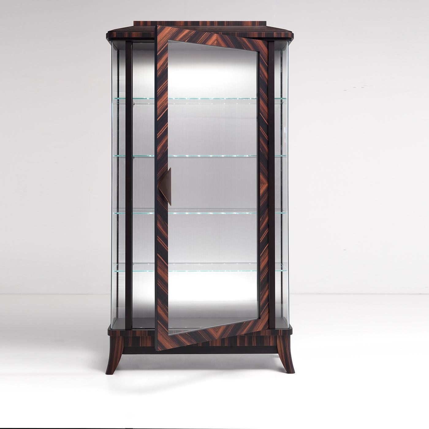 This striking display cabinet effortlessly merges modern and classic influences for a result of undeniable allure. Fashioned of Makassar ebony, the imposing frame stands on four curved feet and the single door in clear glass reveals the inner unit