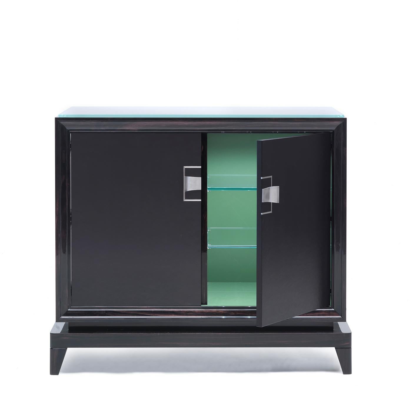This luxurious two-door bar cabinet in Makassar ebony features two internal shelves in clear glass designed to elegantly store cocktail equipment and exquisite collections of glasses. The sophisticated silhouette that it bears is a triumph of the