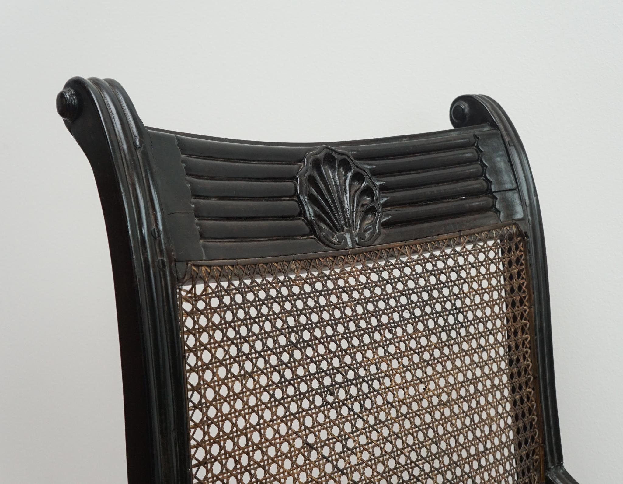 Der hier gezeigte Großvater-Stuhl mit Muschelmarke stammt aus Ceylon, ca. 1820.  Mit seinem exquisit geschnitzten Ebenholzrahmen - der sich durch ein Muschelmarkendetail auf der oberen Schiene auszeichnet - und der von Hand gepolsterten Sitzfläche