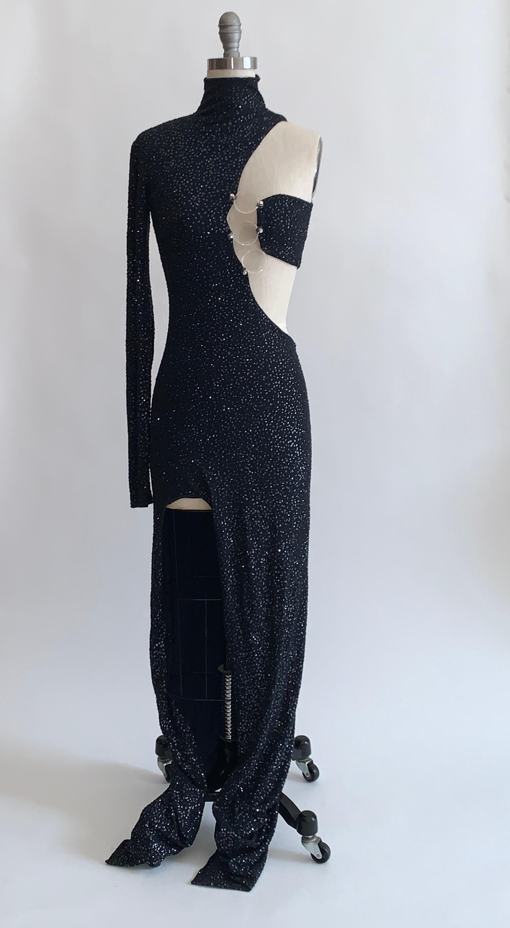 Stunning black gown purchased from the collection of the Ebony Fashion Fair. Black asymmetrical maxi length dress is encrusted with glitter dots and features a one shoulder design with high neck and cut out detail that fastens at bust with three