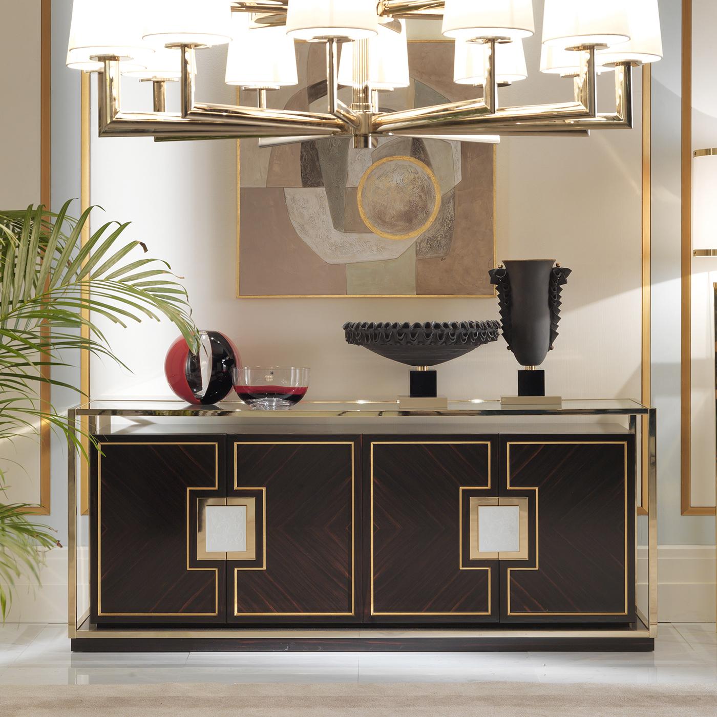 This elegant sideboard boasts a design inspired by the bold sophistication of Art Deco. Its rectangular silhouette, crafted of striking ebony, is enclosed in a brass frame resting on an ebony plinth base. The top and two handles are in frosted,