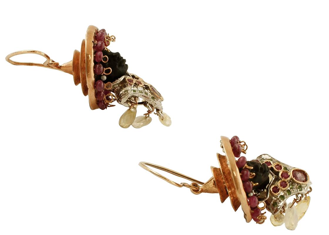 Vintage Moretto earrings in 9k rose gold and silver structure, with ebony face, silver chest studded with diamonds, rubies and dangles of topaz and rock crystal, and with a golden hat embellished with rubies.
The origin of these earrings dates back