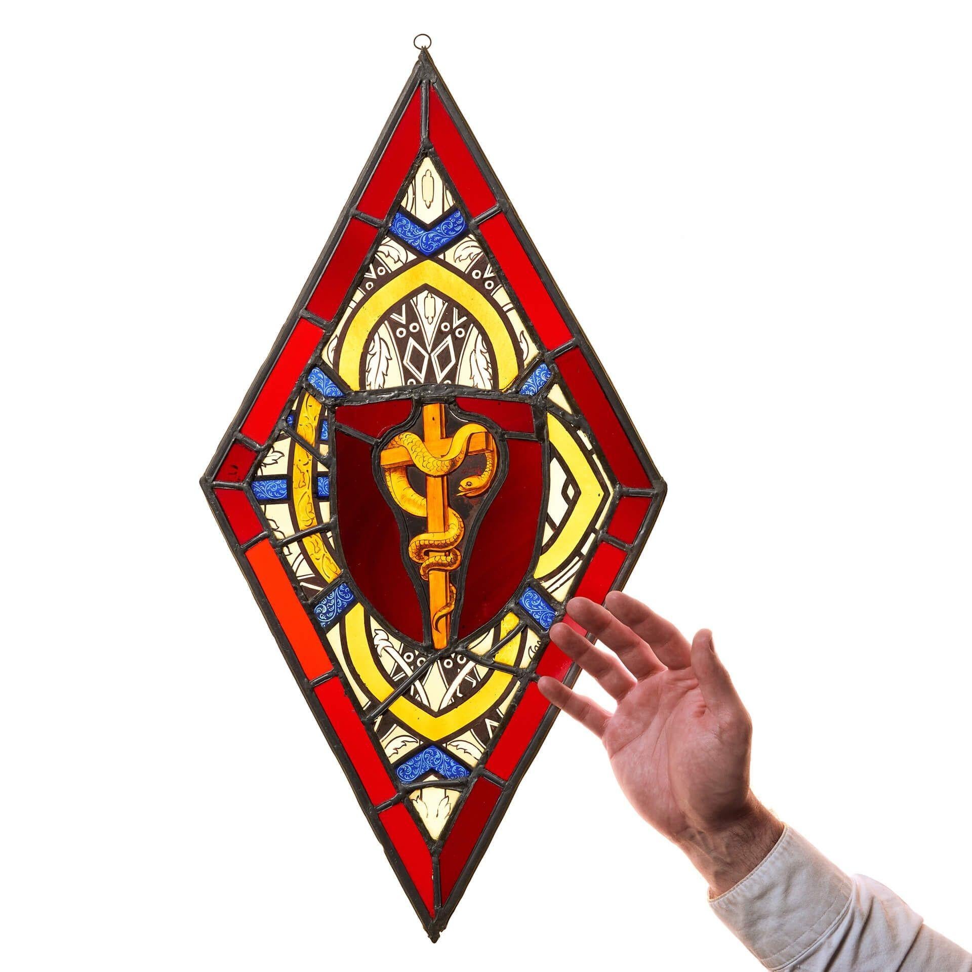Petit panneau de vitrail du XIXe siècle en forme de losange ou de diamant, centré sur un serpent sur une croix. Le serpent est entouré de verre bleu et jaune dans un cadre de vitrail rouge. Parfait pour être accroché à une fenêtre ou devant une