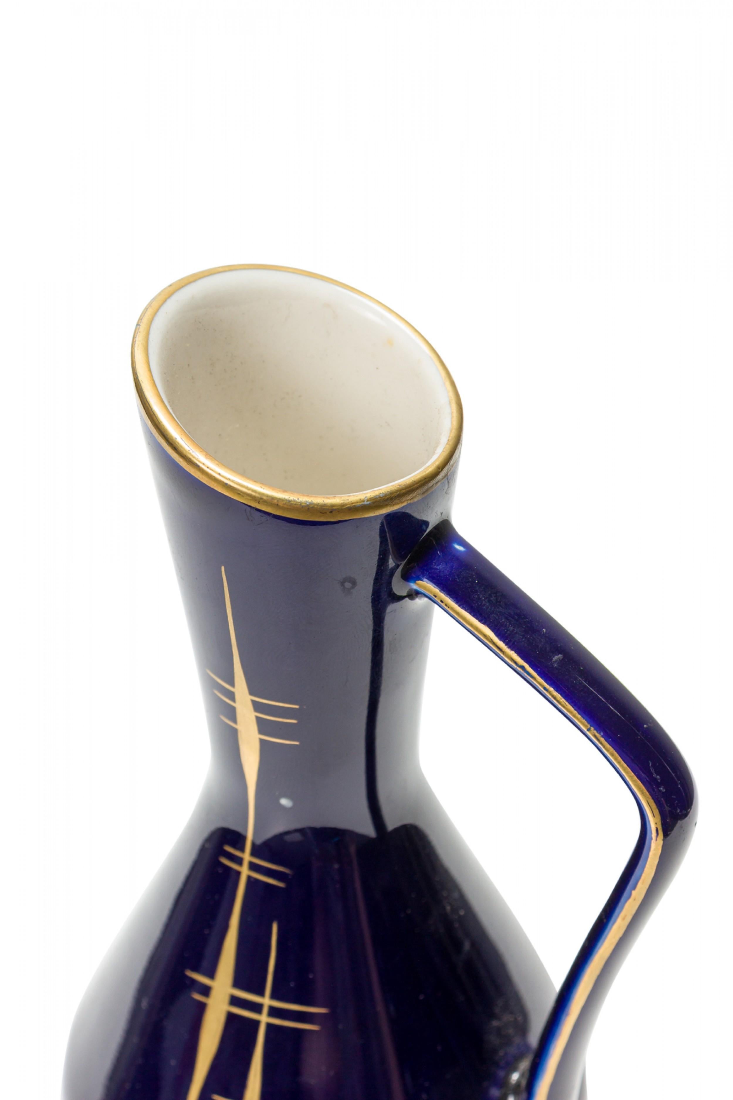 German Mid-Century ceramic pitcher with a diamond form, slanted mouth, and angular handle with a vertical feathered gold line design against a dark cobalt blue glaze. (mark on bottom, HANDMALEREI ECHT KOBALT).