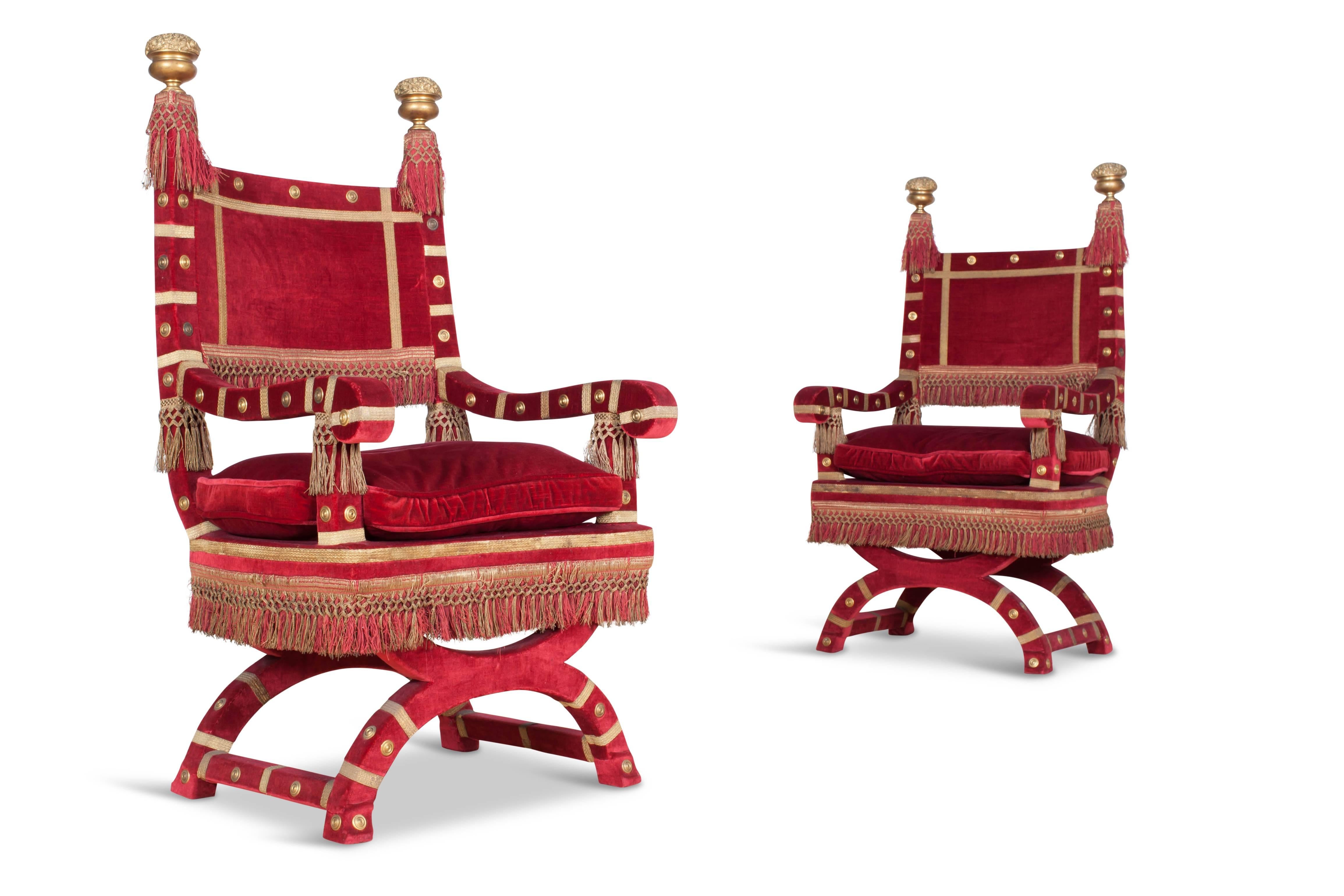 Hollywood Regency style exuberant and decorative pair of armchairs, Italy, 1940s. 

The chairs are upholstered in rich red velvet, with gold details and floss decorations. The tops of the backrests are decorated with two large floral ornaments in