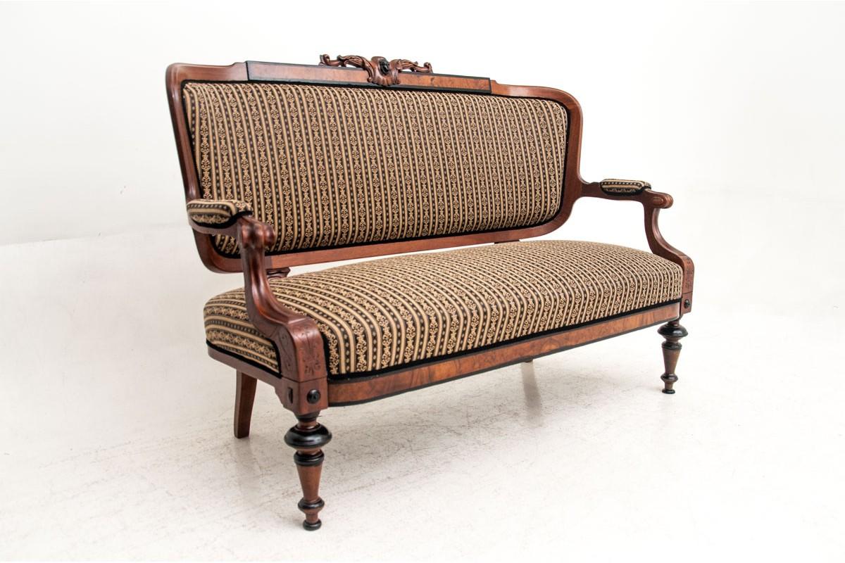 The antique sofa was made at the turn of the century in mahogany. Seat, backrest and partial armrests upholstered in fabric, stile subtly decorated with carvings. Very good condition, all supported on turned, stable legs. The restoration is