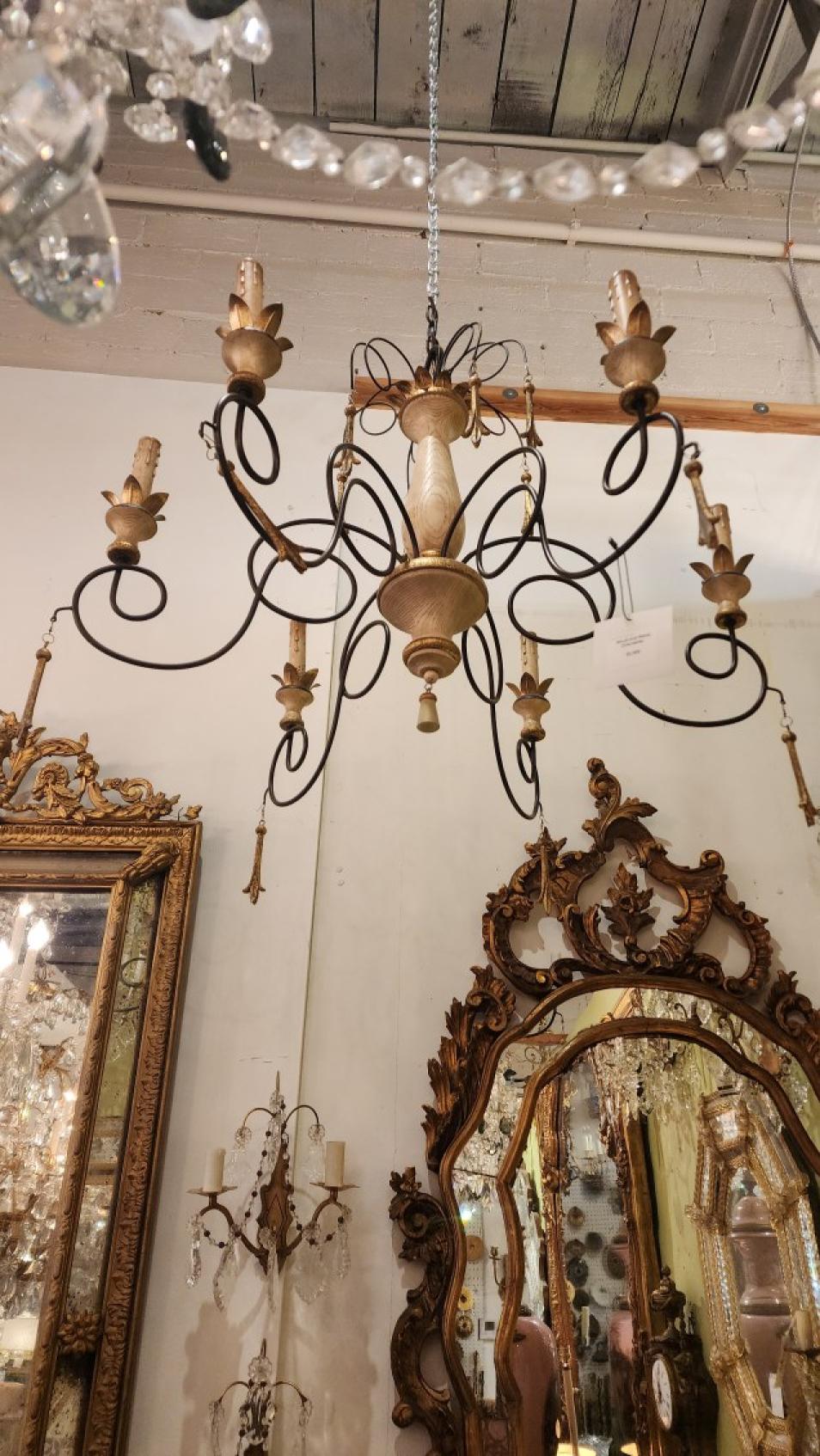 Questo splendido lampadario fonde il fascino rustico del Mediterraneo con l'eleganza italiana, creando un pezzo versatile ed eclettico. Caratterizzato da una combinazione di ferro battuto e legno dorato, fonde il metallo scuro con elementi in legno