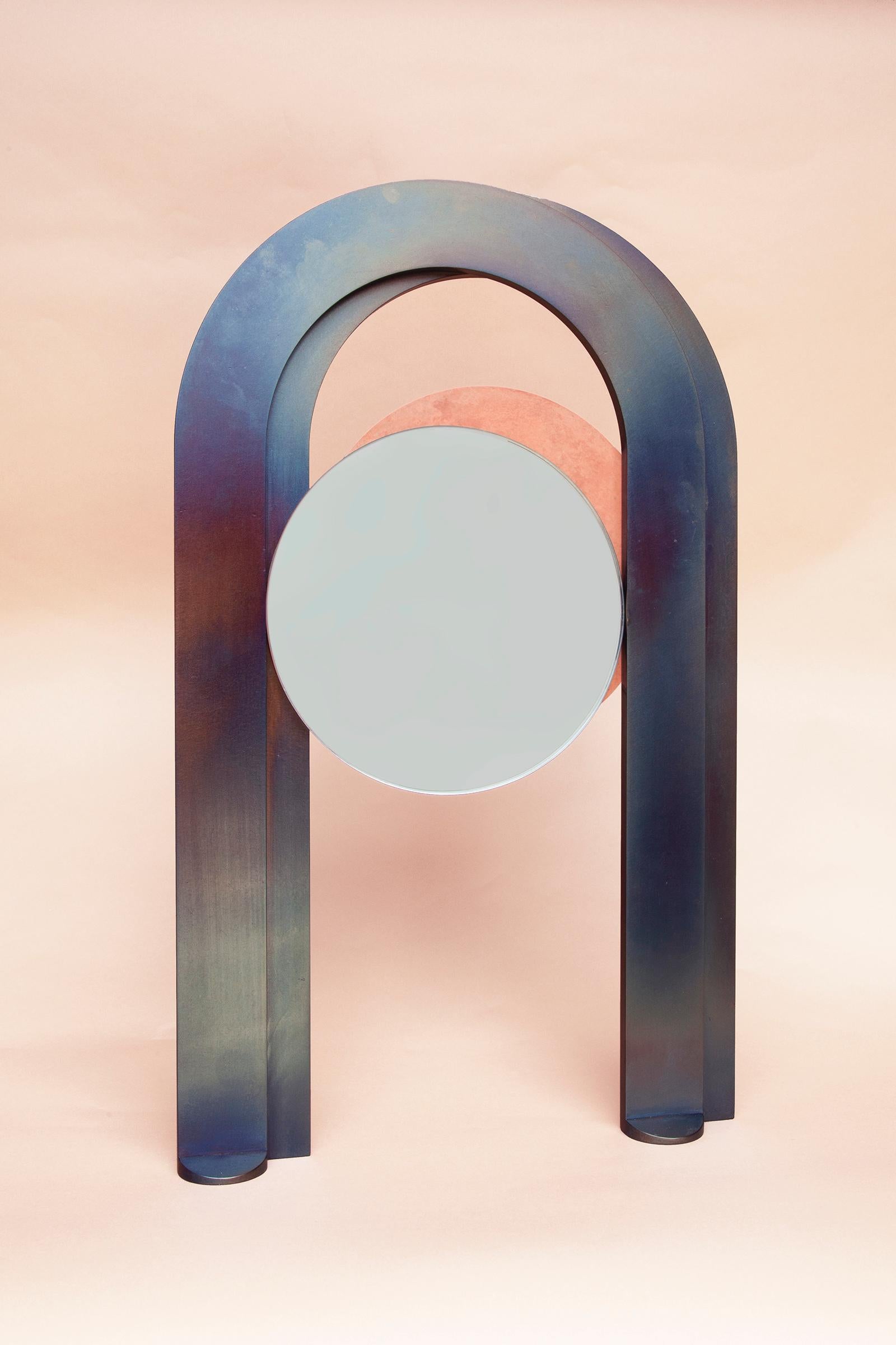 A pair of offset tempered steel arches frame two eclipsing mirrors, shifting to reveal textured patina plates. Like two intersecting celestial bodies, the partnered mirrors suspend delicately within their frame leaving space for the gaze to travel