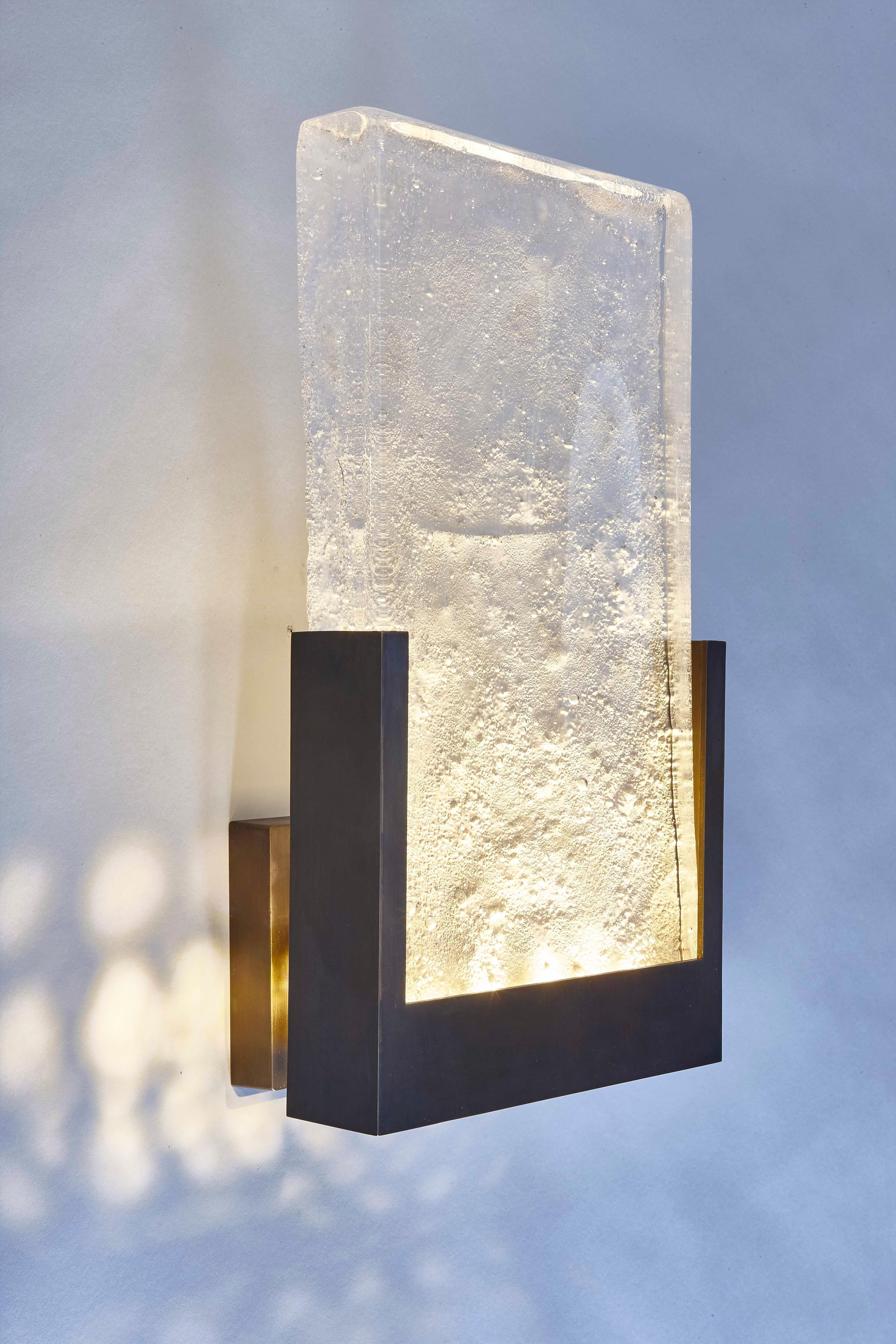 The wall light version of our Eclipse Chandelier. This stunning handcrafted light has strong lines giving a bold statement to any room. The hand-cast glass panel representing the surface of the moon, sits in a bronze frame and creates a wonderfully