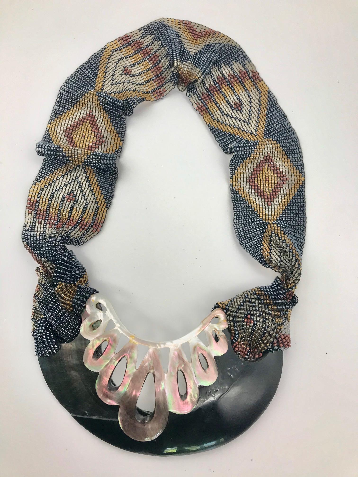 This Statement Necklace is eco-luxe and sustainable.
The materials used are iridescent mother of pearl/nacre and  black
resin ,enhanced by  hand carved mother of pearl piece from Bali , and
hand beaded decorated strap also from Bali.This piece of