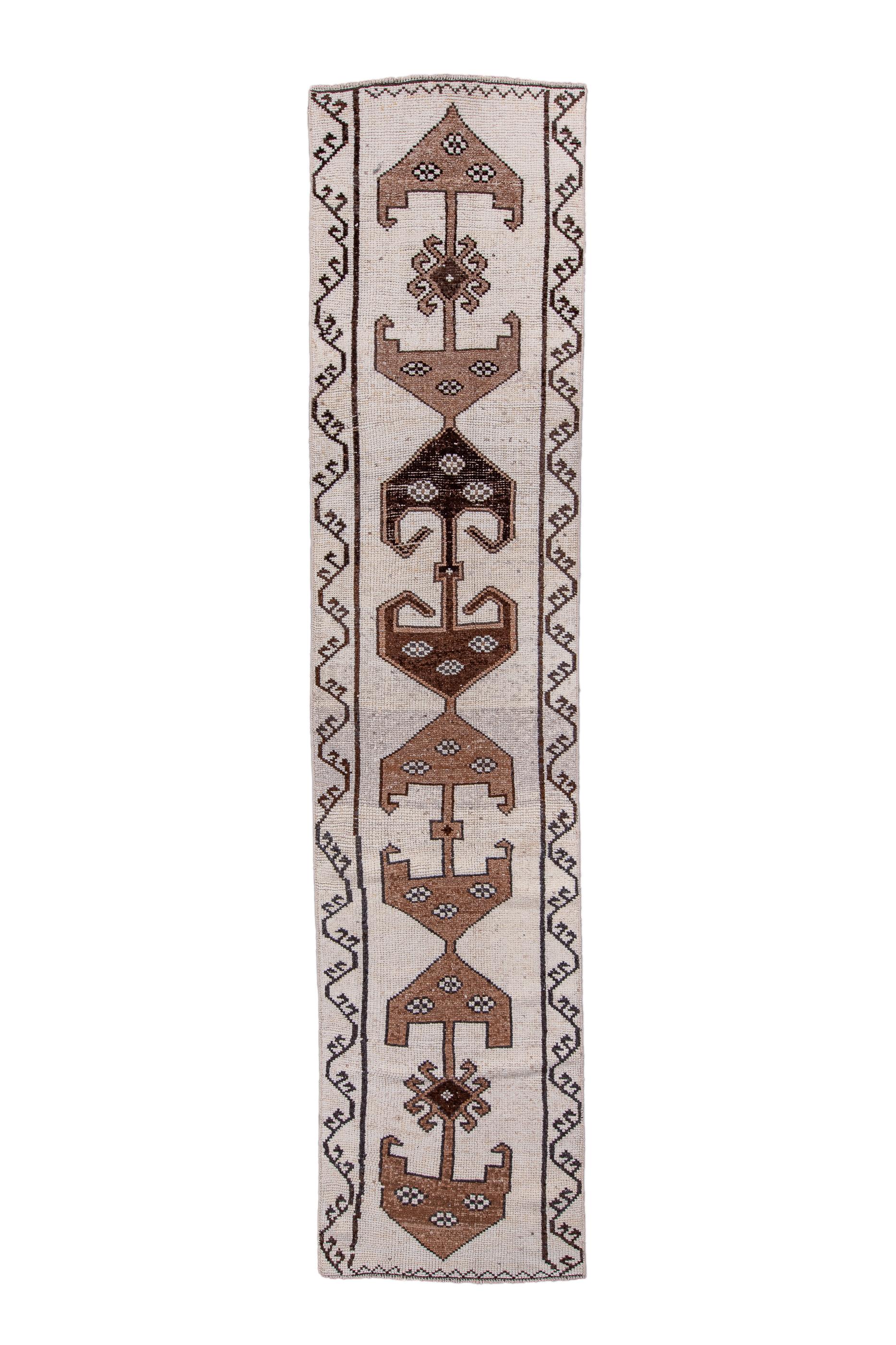 This west Anatolian village kenare (runner) show the currently popular ecru field with a floating pole medallion of red and brown anchor motives, with two smaller hooked diamonds. Ecru main border with lateral, hooked meander, and narrow zig-zags