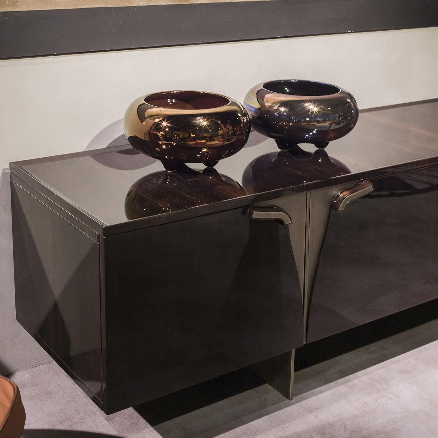 At once stylish and rigorous, this sideboard makes for a superb addition to exclusive living rooms or foyers of modern inspiration. Bronze-finished metal details create a seductive contrast with the linear and almost relaxing veins the eucalyptus