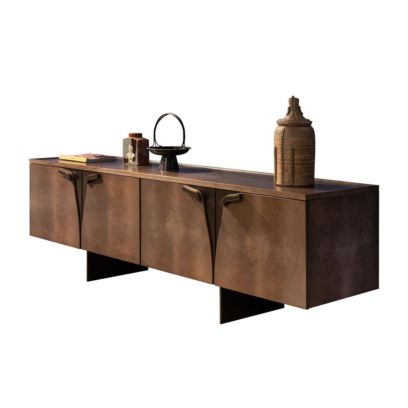 Fluid-lined metal details with a bronze finish interrupt the luxurious uniqueness of this imposing sideboard in prized feathered walnut. Minimalist legs confirm the essential character immediately conveyed through the rigorously sculpted profiles,