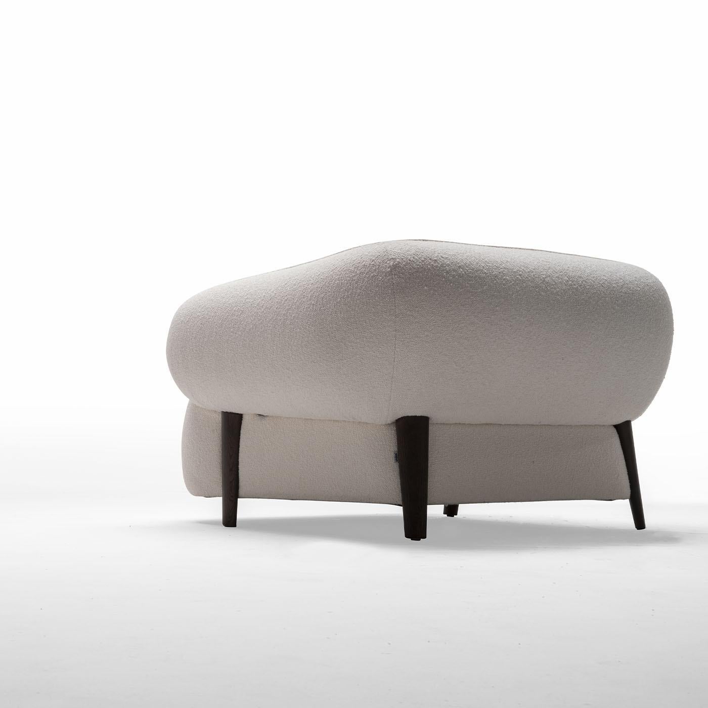 Ideally combined with its pouf counterpart for a cohesive look, this armchair invites one to take moments of pure relaxation embraced by its bold and plump volumes. The sleek gray-stained frame welcomes a wide seat fully enveloped by a single