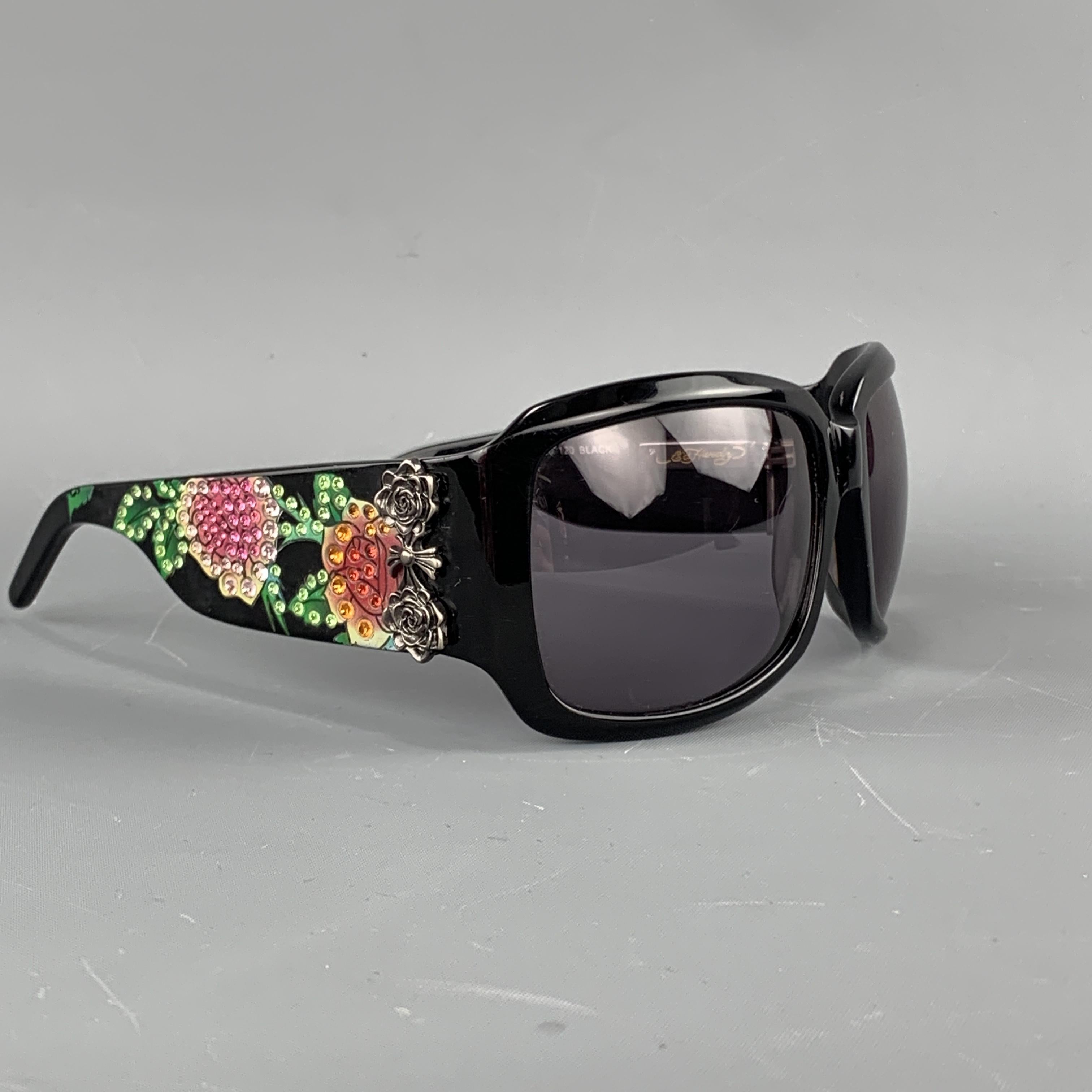 ED HARDY oversized sunglasses come in black acetate with oversized rectangle lenses, dark silver tone metal side adornments, and thick arms with skull and rose graphics studded with Swarovski crystals. Minor wear.

Very good Pre-Owned
