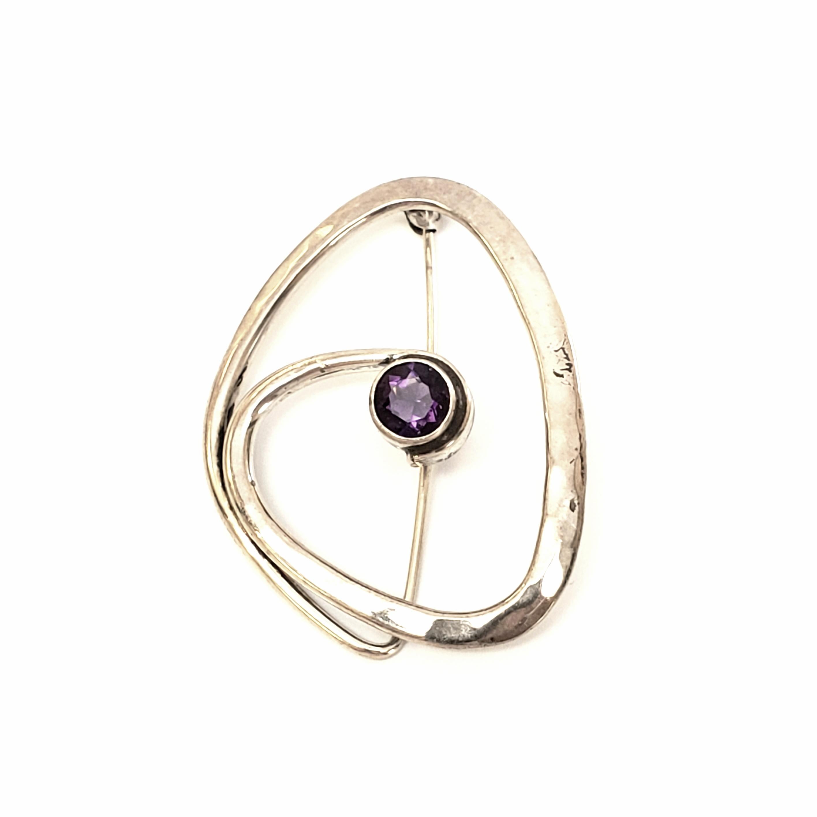 Sterling silver and amethyst pin designed by Ed Levin.

Highly sought after designer, Ed Levin, is known for making wearable art. This modernist design is slightly hammered and features a round, faceted, bezel set amethyst at its center.

Measures 1