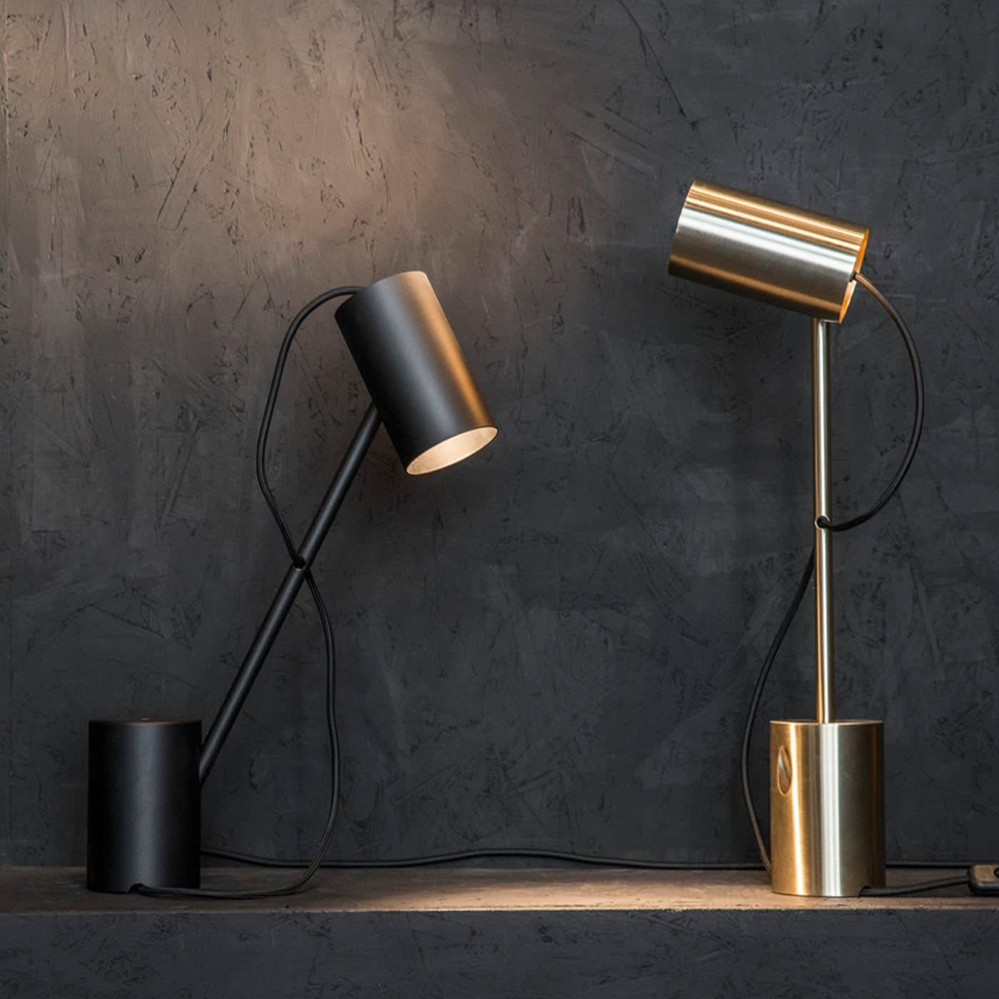 This elegant desk lamp has a metal structure resting on a base of carved solid steel. The cylinder of the base is echoed in the cylindrical shape of the shade. Because of two holes at the bottom, this versatile lamp can be used also as ambient light.