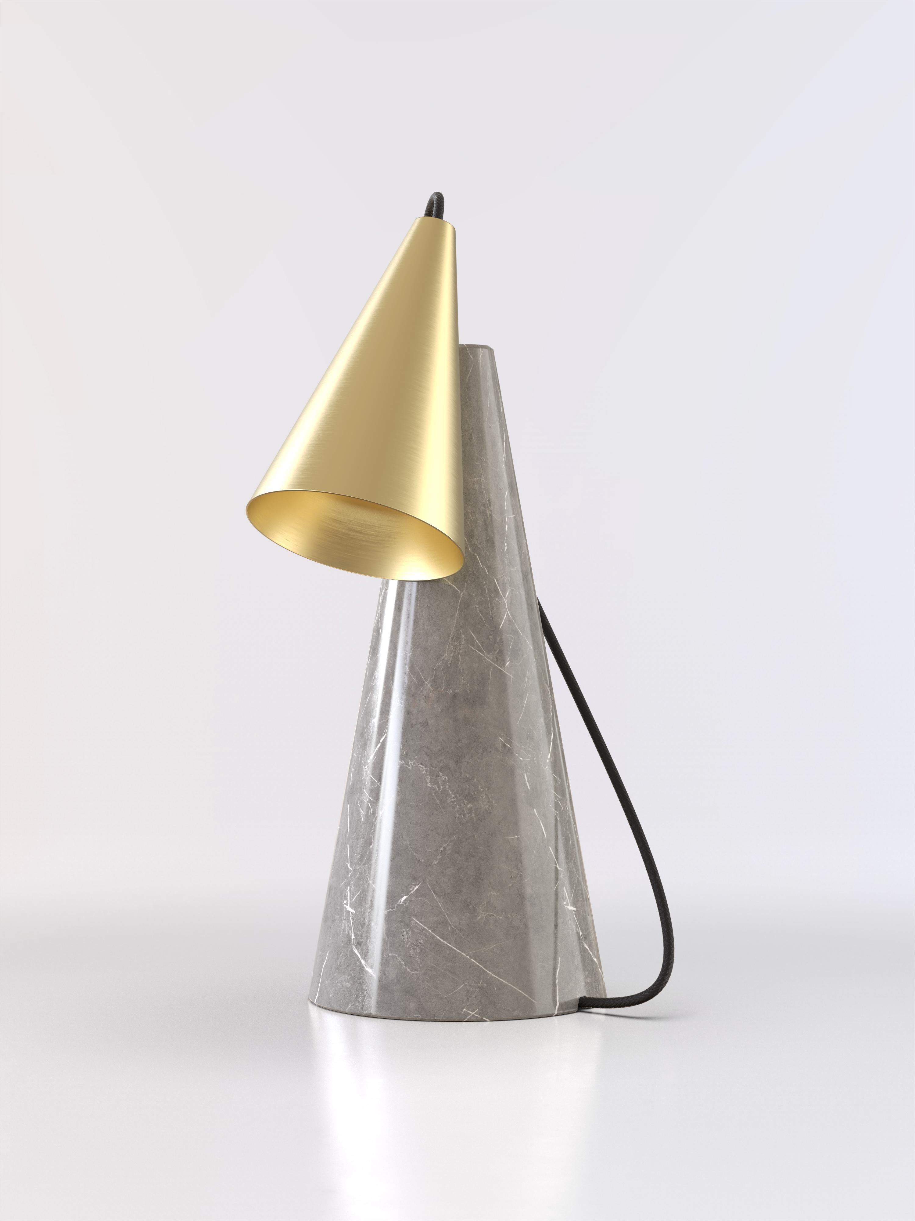 Lámpara de sobremesa con base de piedra gris y pantalla cónica de latón cepillado.