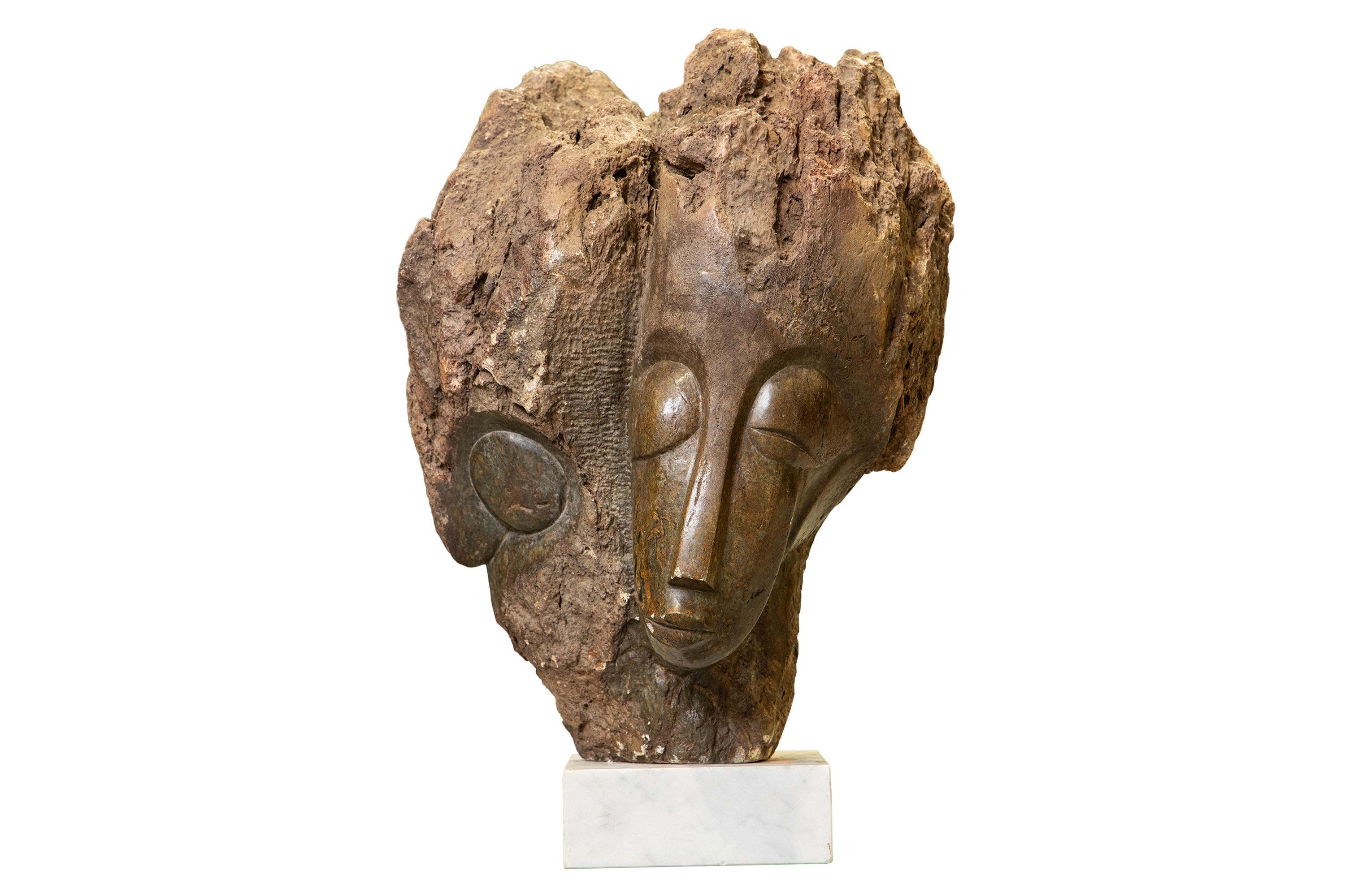 Eddie Masaya (Zimbabwean, b. 1960), Shona sculpture of Twin Faces, opal stone, on a white marble base. The image is of a stone sculpture, likely a Shona sculpture from Zimbabwe, potentially created by artist Eddie Masaya. The sculpture is carved