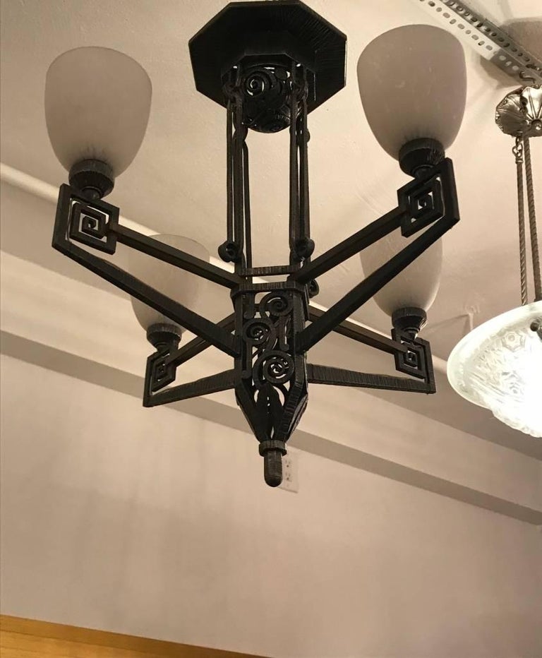 Beautiful French Art Deco chandelier in the style of Edgar Brandt. Having intricate deco hand-forged iron frame details. With four glass tulips pointing upwards.