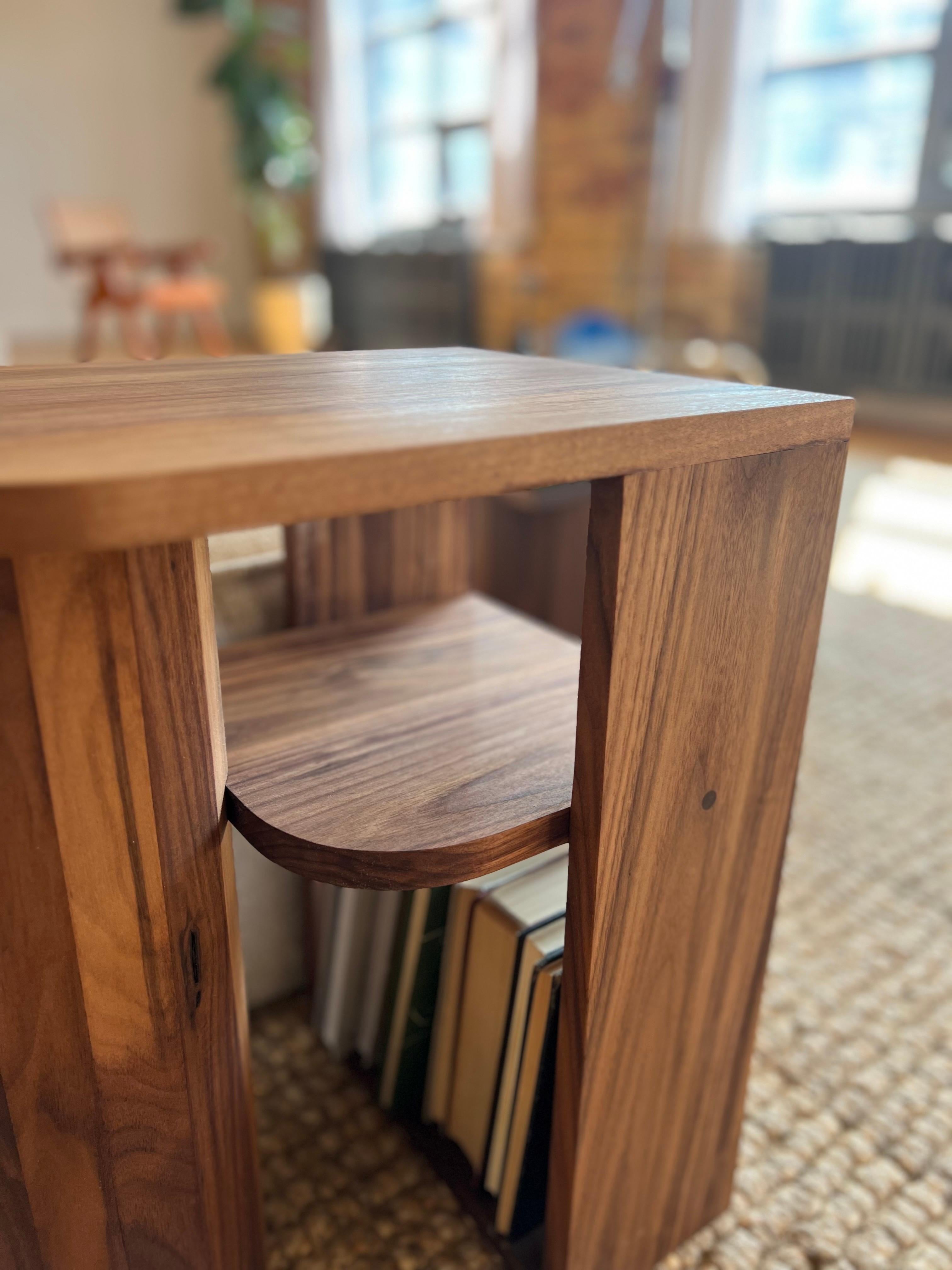 Realizzato a mano in noce massiccio, questo tavolino è funzionale e scultoreo allo stesso tempo. La sua audace forma geometrica è caratterizzata da un centro aperto con un ripiano incorporato, che offre un posto per libri, dischi o oggetti