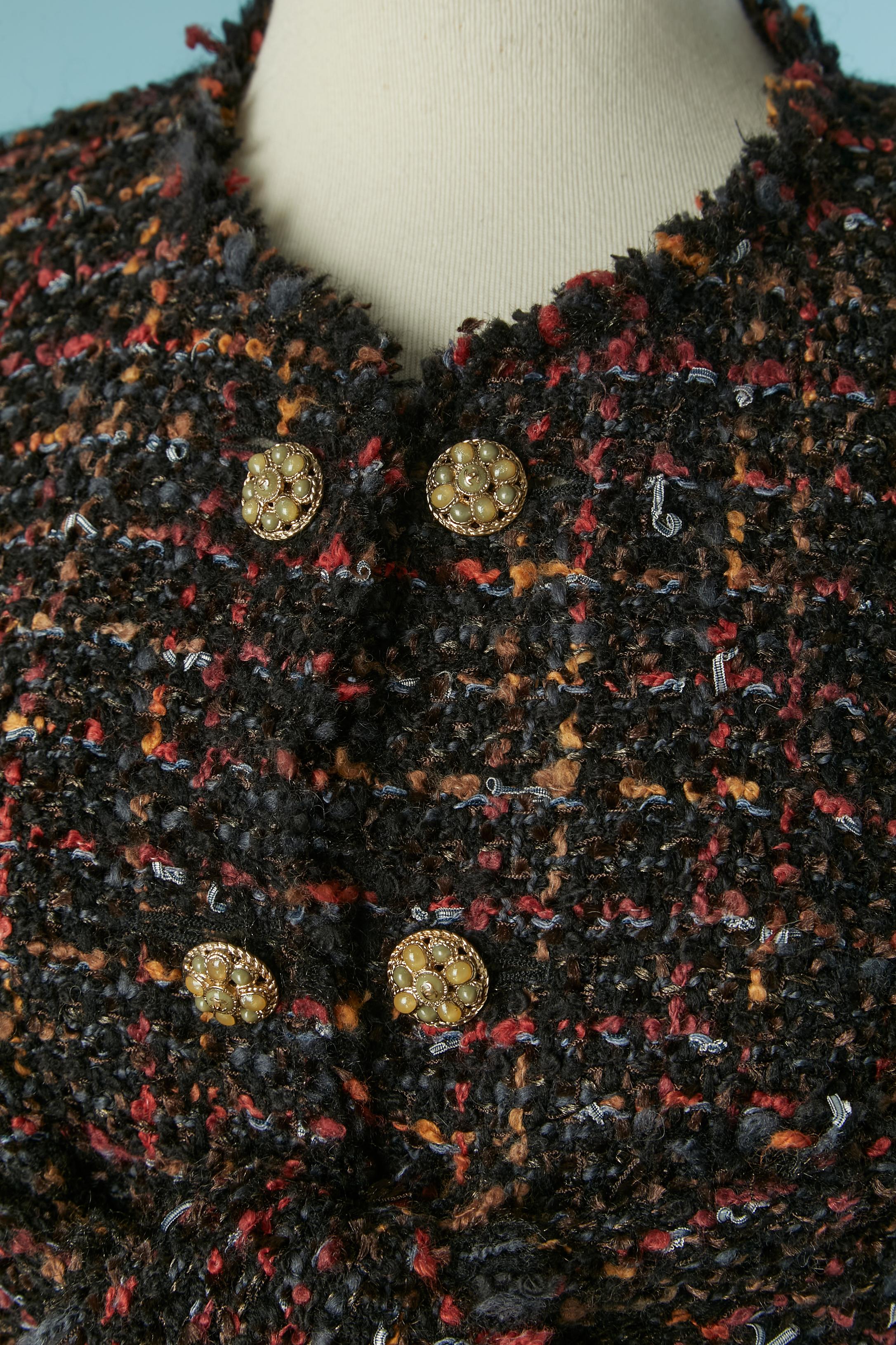 Tweed-Jacke von Rand zu Rand mit unter der Brust gebundenem Schal. Zusammensetzung des Tweeds: 48% Wolle, 27% Acryl, 19% Nylon, 5% Viskose, 1% Leinen. Futter mit Markenzeichen aus Seide. 
Schulterpolster. Knopf, Kette und Knopflochverschluss in der