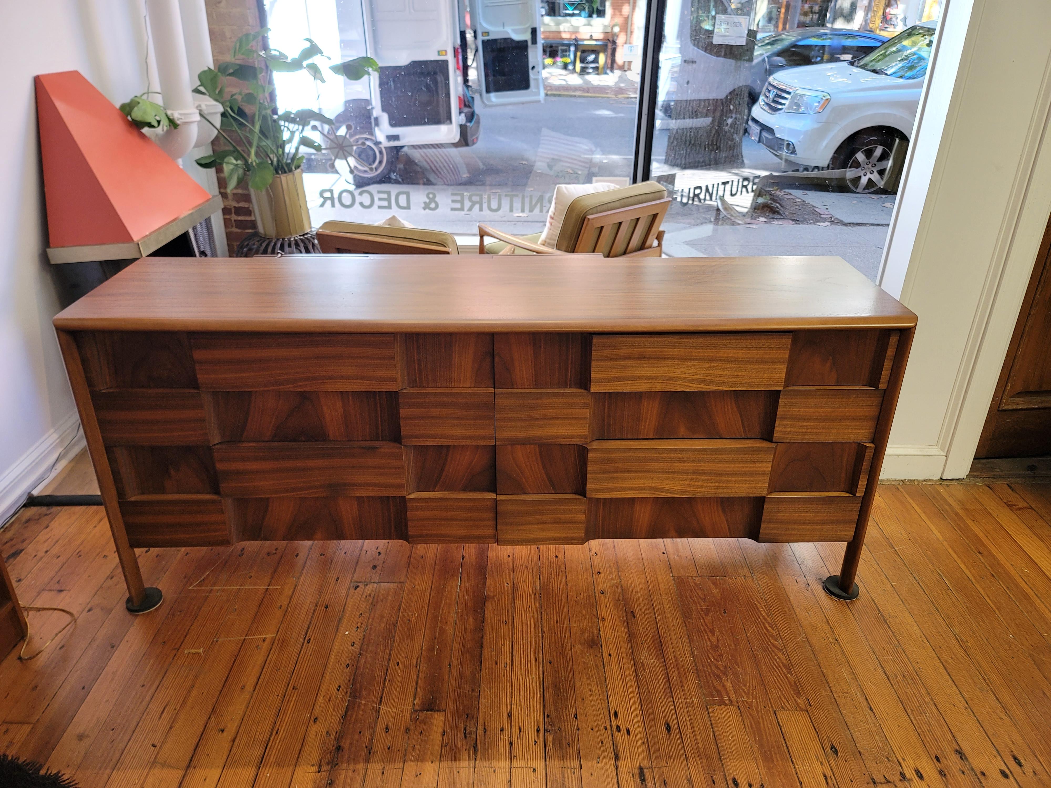 This walnut dresser with unusual sculpted drawer fronts is often referred to as the Checkerboard line designed by Edmond Spence. The quality is apparent with the bookmatched walnut drawer fronts and solid construction. Absolutely stunning example of
