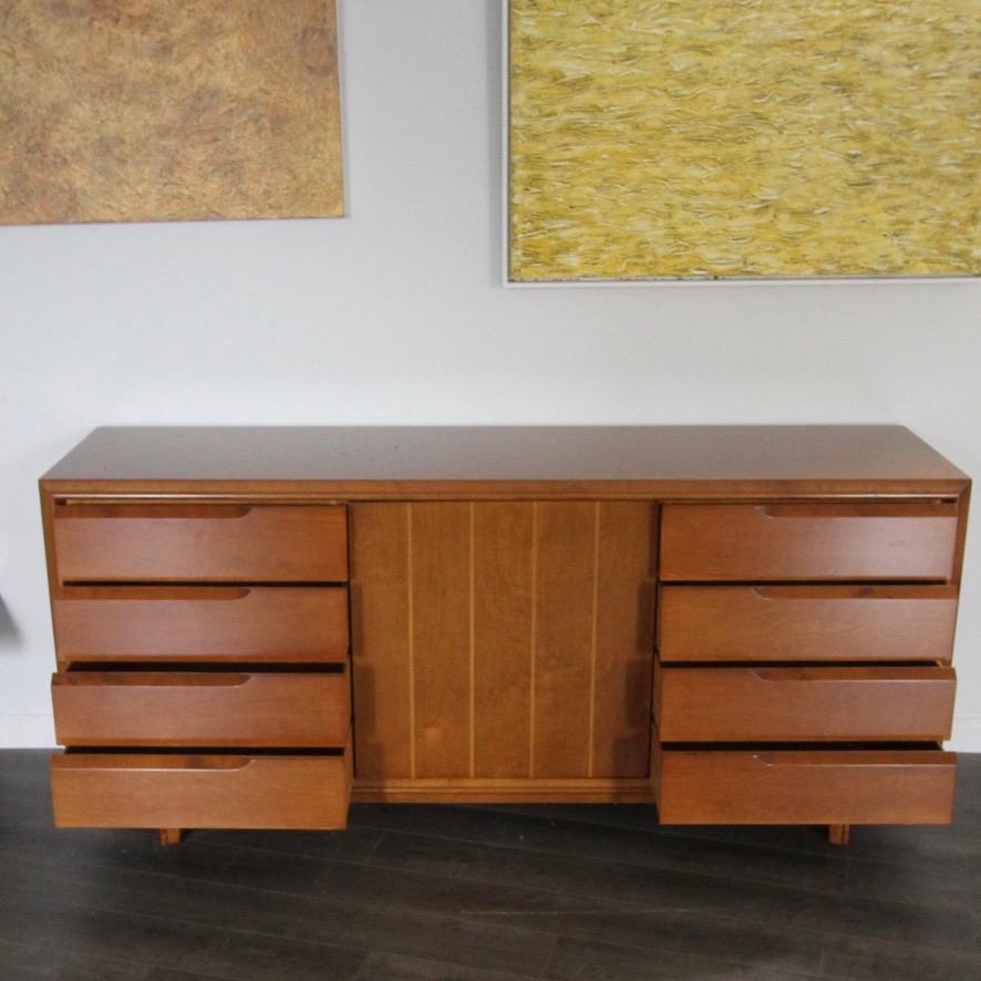 Freshly refinished is this 60s era credenza/sideboard designed by Edmond J. Spence. With four dovetailed drawers on each side and a middle door with two shelves and a silverware drawer atop.