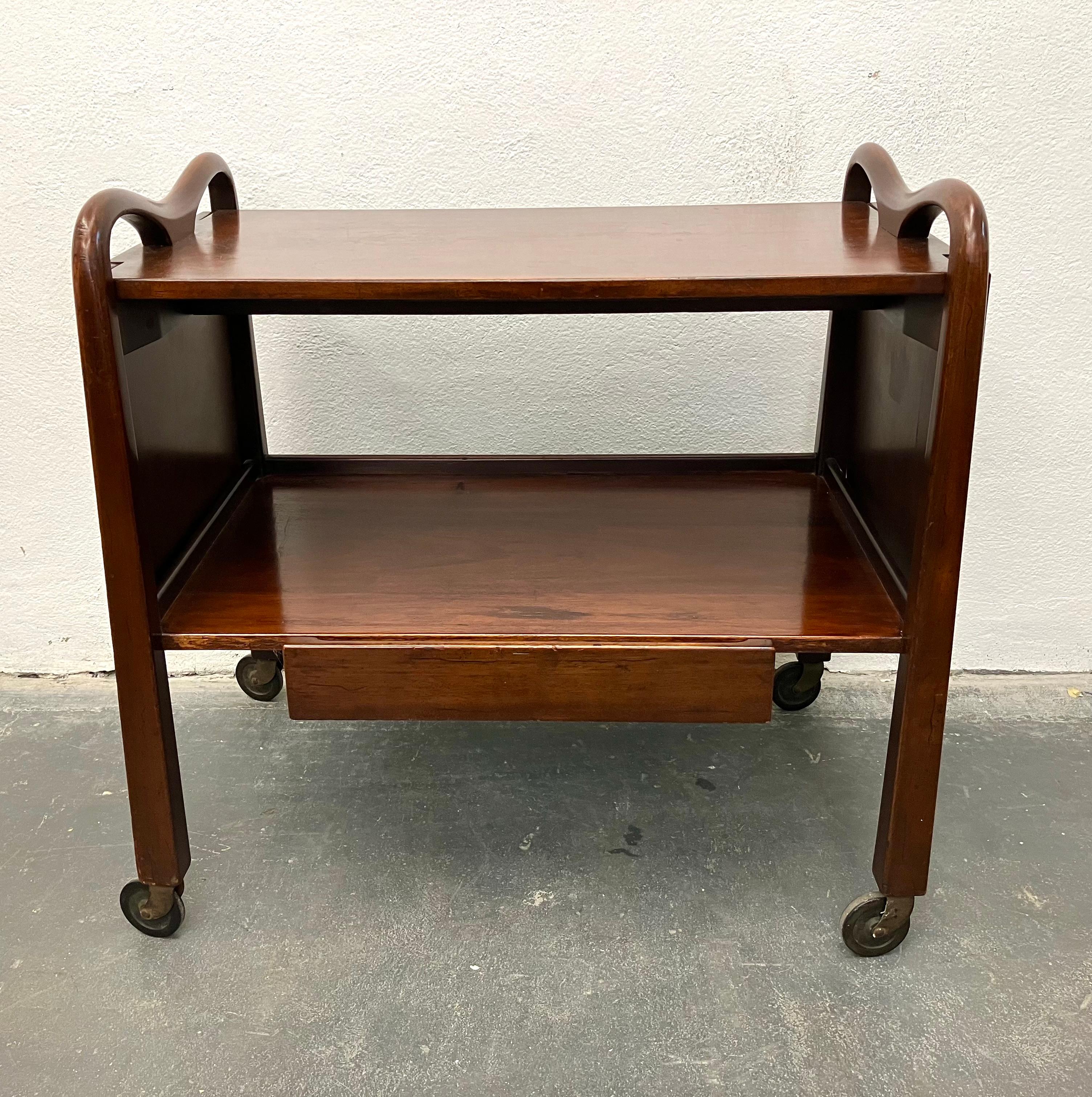 Cuban mahogany rolling bar cart with inverse tapered legs, carved handles, one drawer, and two drop-leaf extensions. Designed by American designer Edmund J. Spence in a stylized Mexican Modern pastiche, and made in Mexico by Industria Meublera.