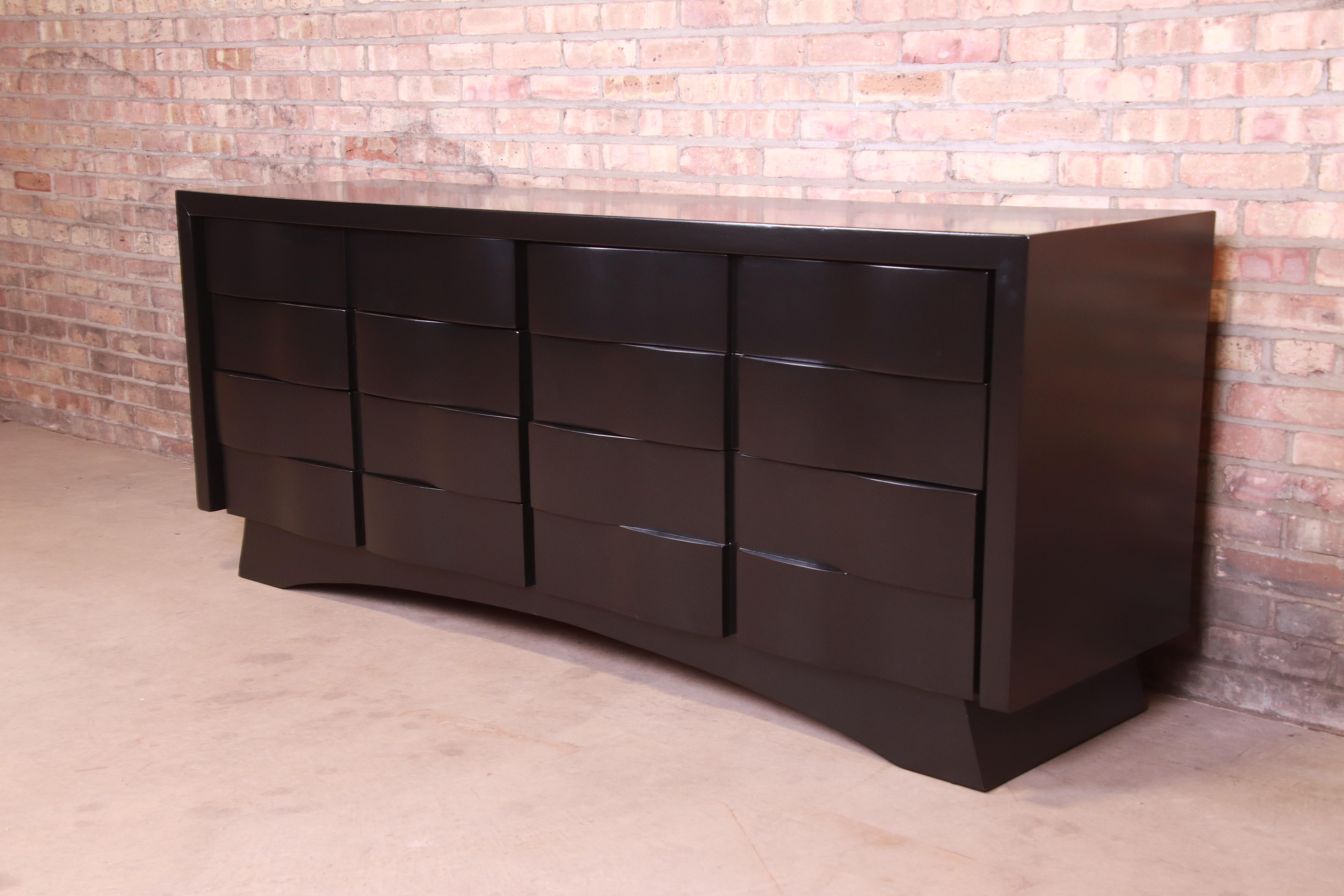 An exceptional Mid-Century Modern sculpted wave front black lacquered long dresser or credenza

In the manner of Edmond J. Spence

Mid-20th century

Measures: 76.63