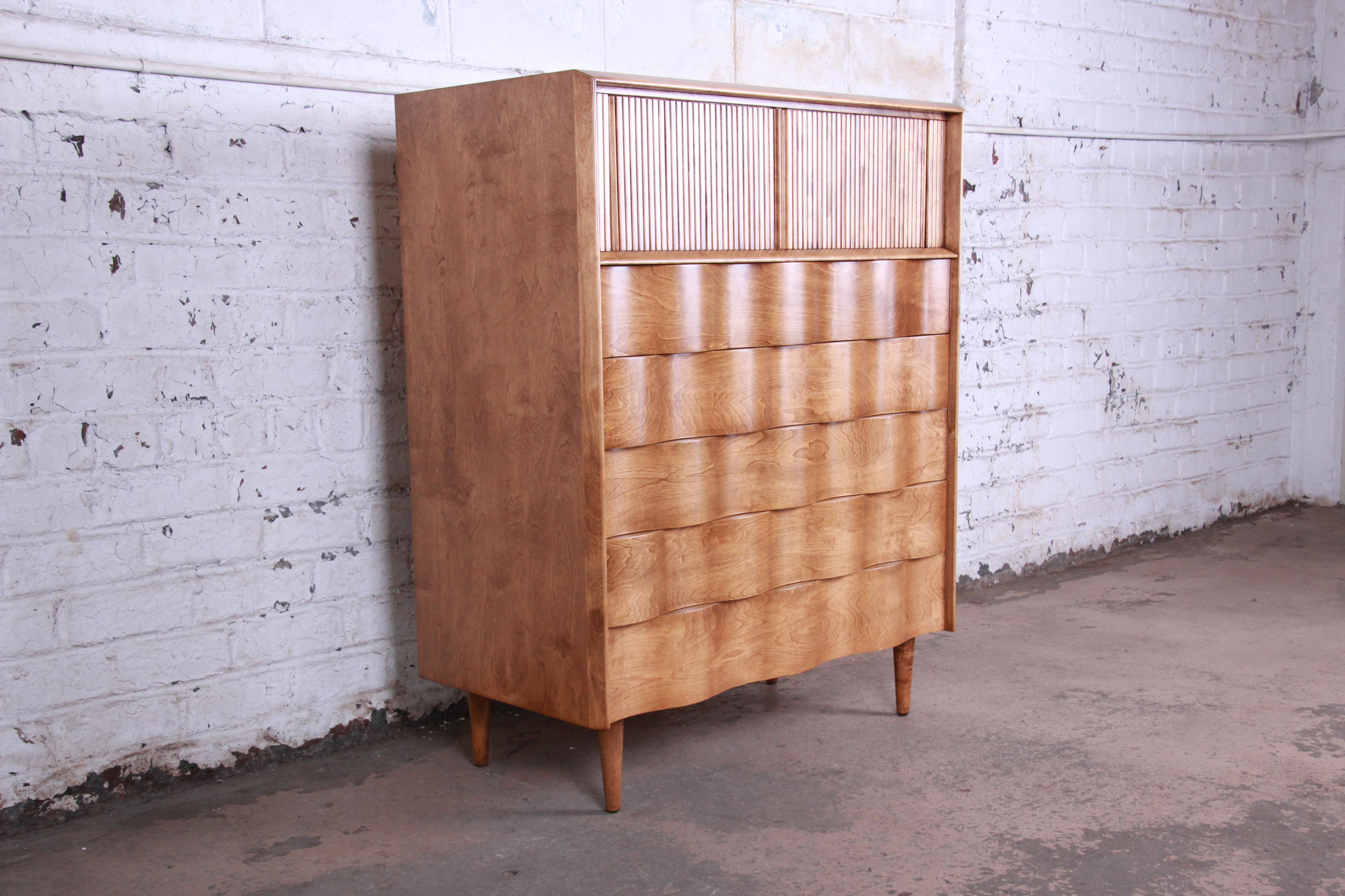Offering a rare and exceptional Mid-Century Modern wave front highboy dresser designed by Edmond Spence. The dresser features a unique wave Front Design and stunning birch wood grain. It offers ample storage good storage deep dovetailed drawers.