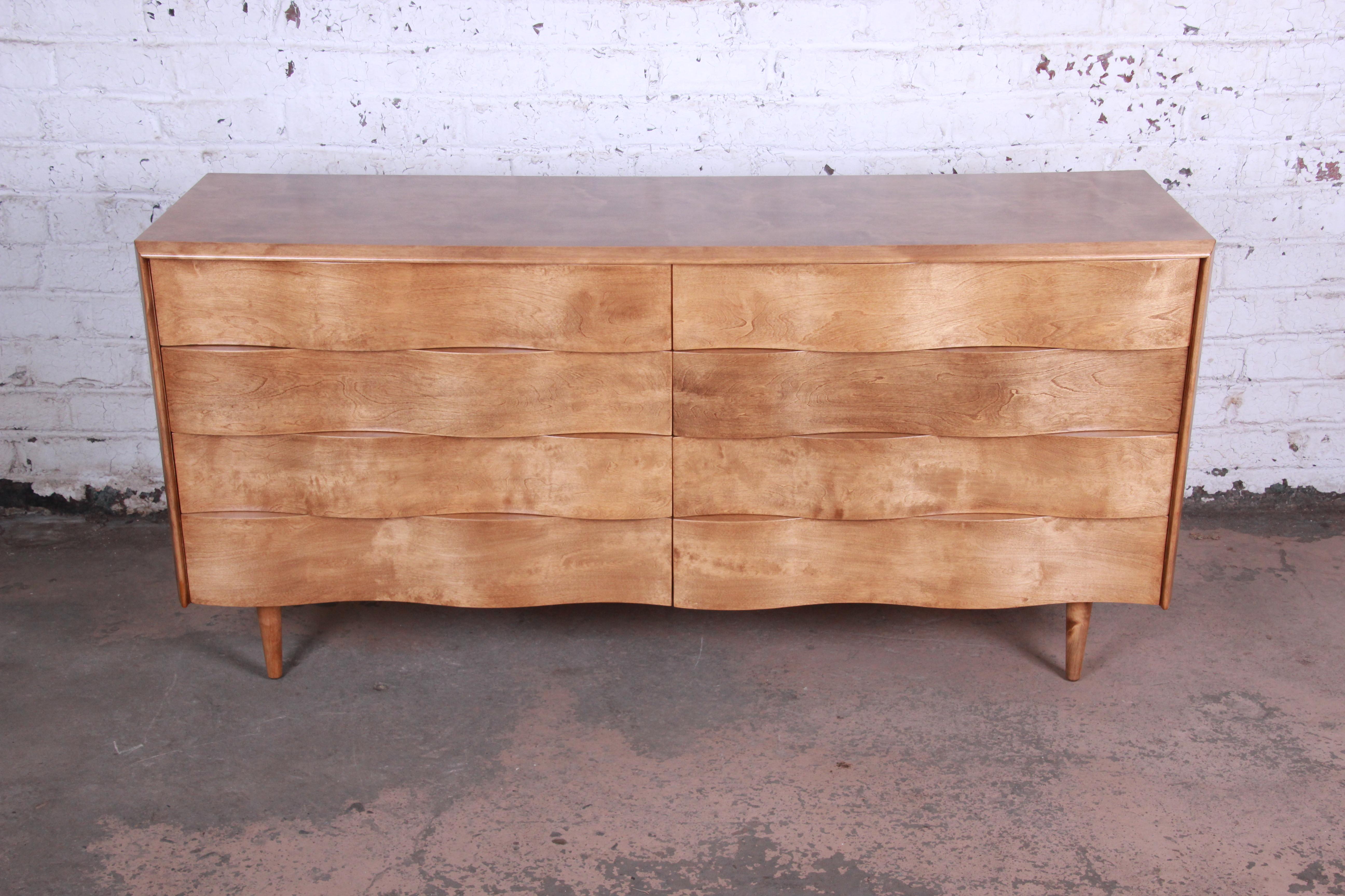 Offering a rare and exceptional Mid-Century Modern wave front long dresser designed by Edmond Spence. The dresser features a unique wave front design and stunning birch wood grain. It offers ample storage good storage deep dovetailed drawers. The