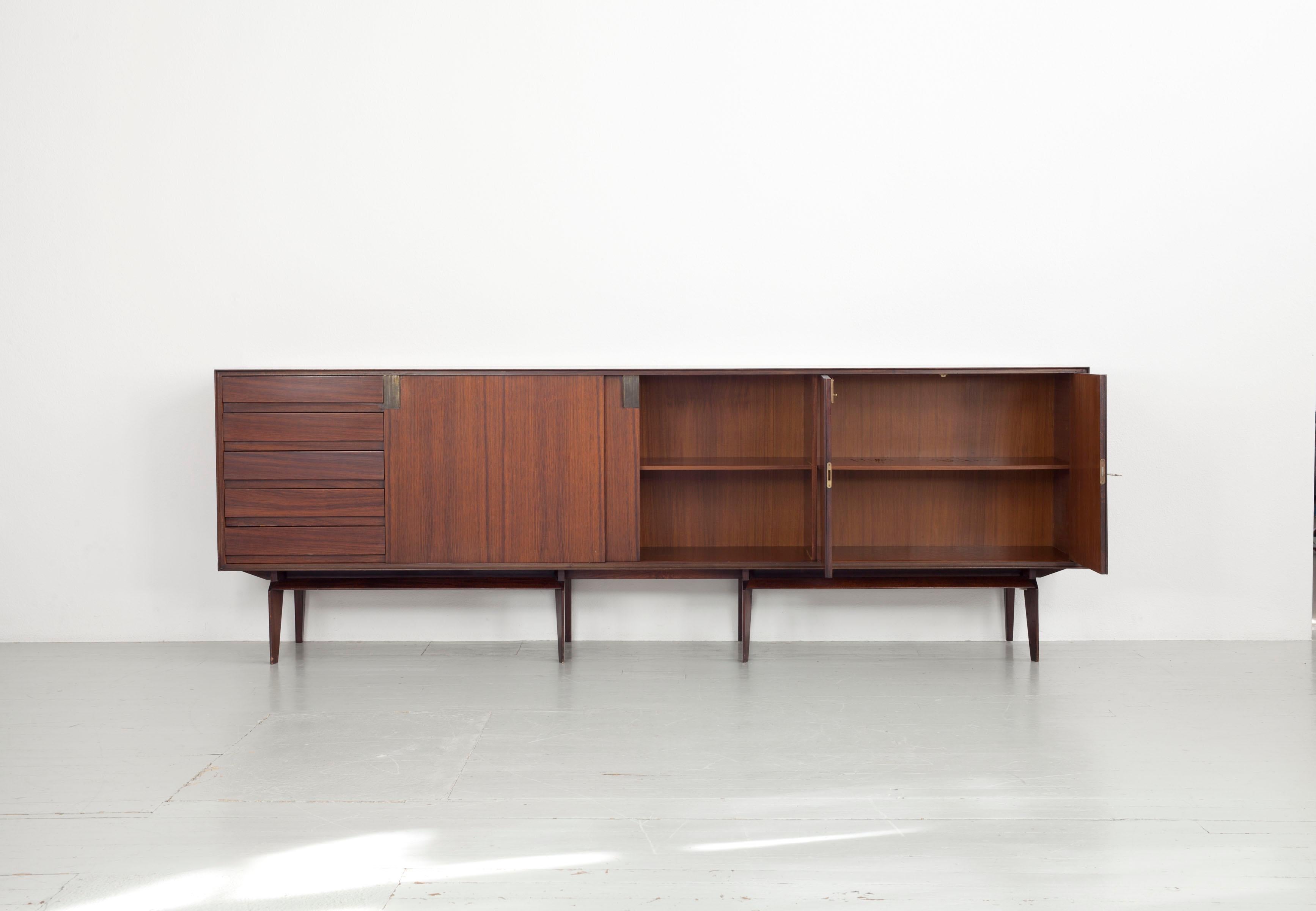 This Italian sideboard dates back to the 1960s. The sideboard was designed by Edmondo Palutari and manufactured by Dassi Lissone. The board is made of rosewood and has two sliding doors, a large hinged door and several drawers. Except for some