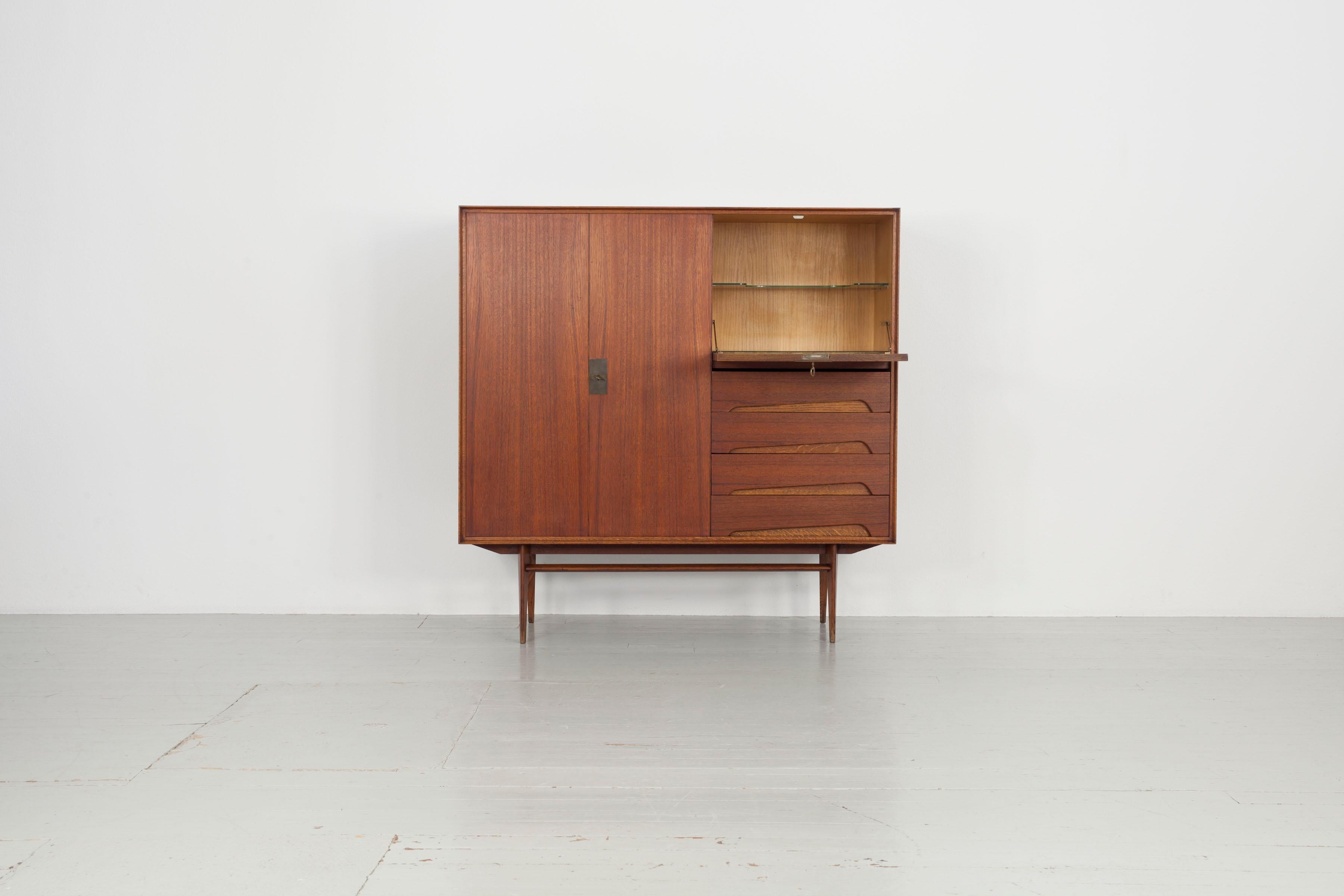 This sideboard has been crafted with teak and brass detailing. The drop-leaf door on the right hand side allows the sideboard to also function as a secretaire. The versatile sideboard offers plenty of room for storage, and remains in a very good