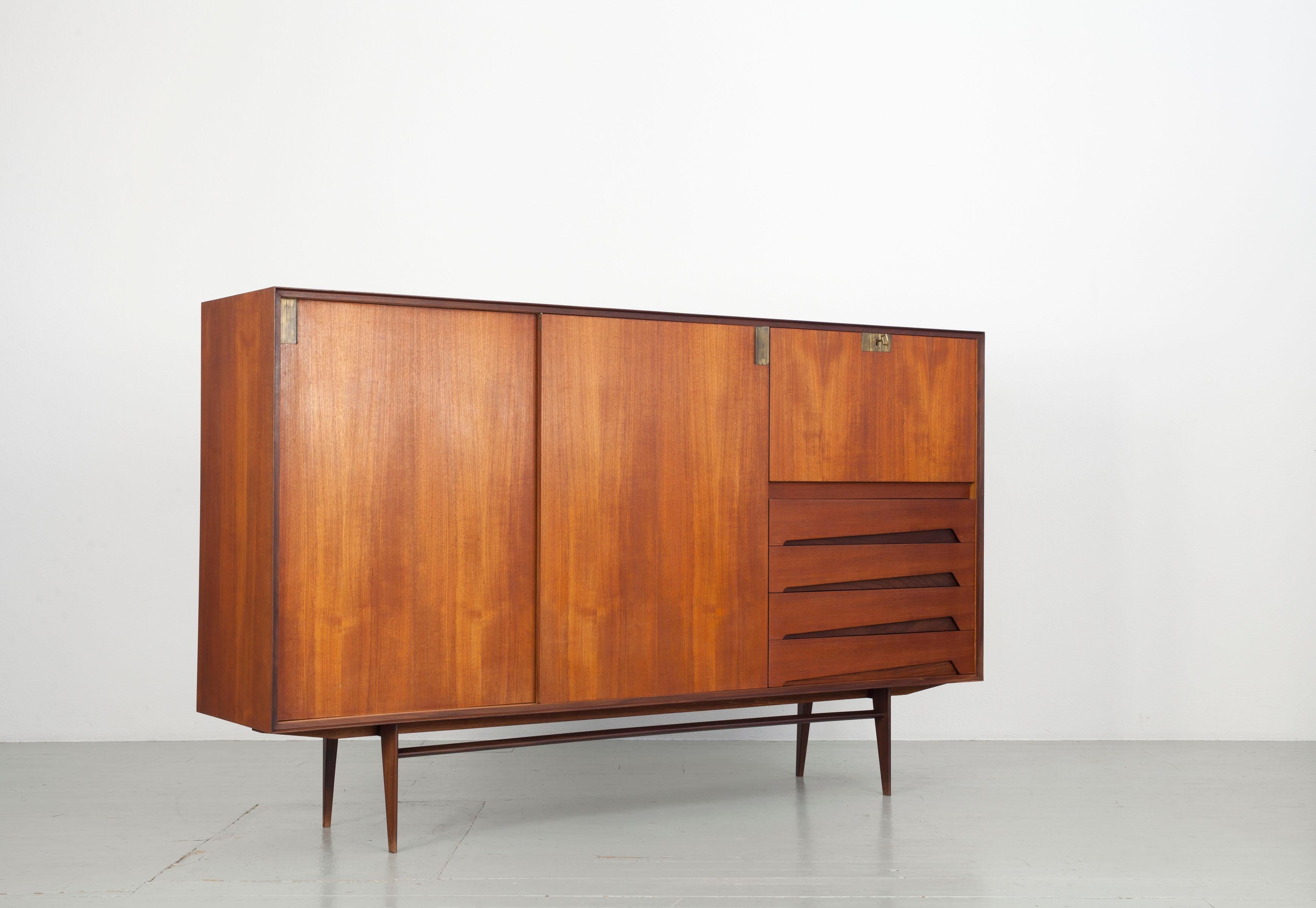 This sideboard is made of teak and finished with brass details. It can also be used as a secretary through the door on the right side of the closet. The versatile sideboard offers plenty of storage space.

Edmondo Palutari worked in-house at Dassi
