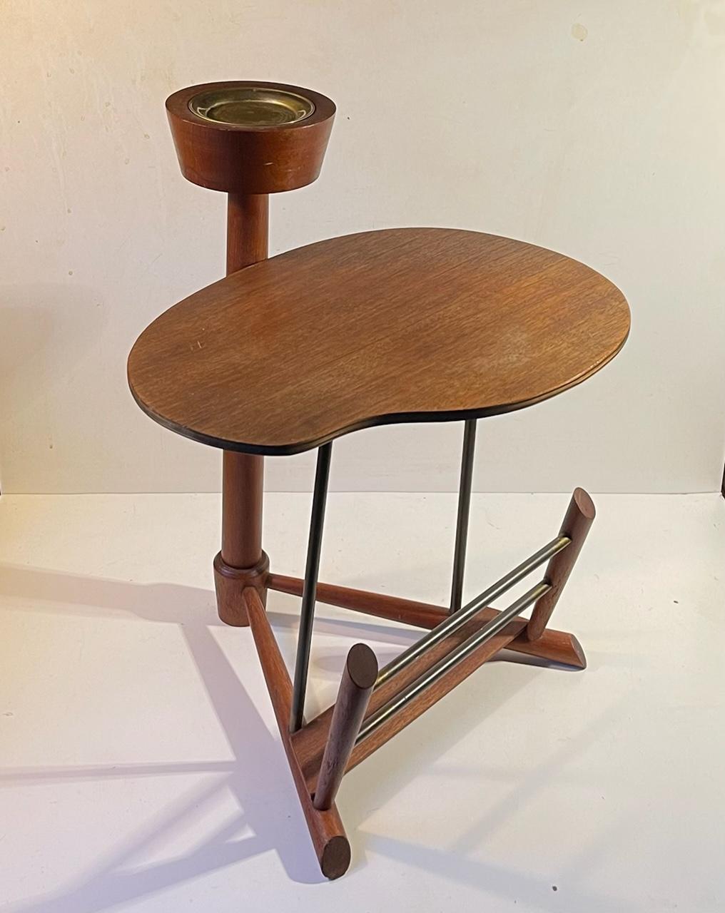 Small light-weight hybrid side table made from teak and brass. It features a kidney shaped table top, a magazine rack and a removable ashtray or coasters for your morning tea or coffee. It was made by Edmund Jørgensen in Denmark during the late