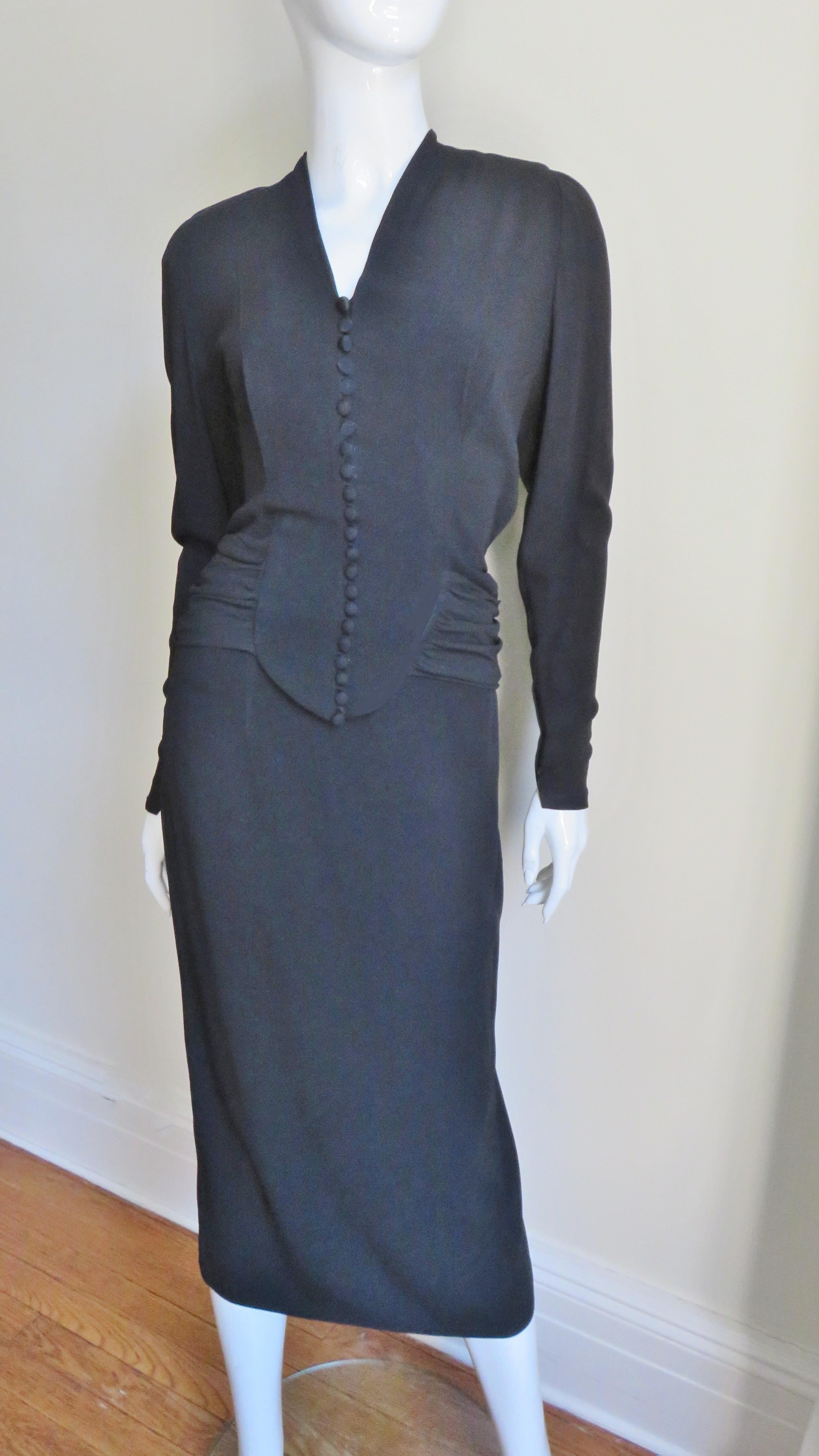 A beautiful elaborately detailed top and skirt from notable 1940s American designer Edna Vilm.  It consists of a hip length long sleeve top with with zipper cuffs, a V neck, padded shoulders and front buttons and loops. The back is stunning with