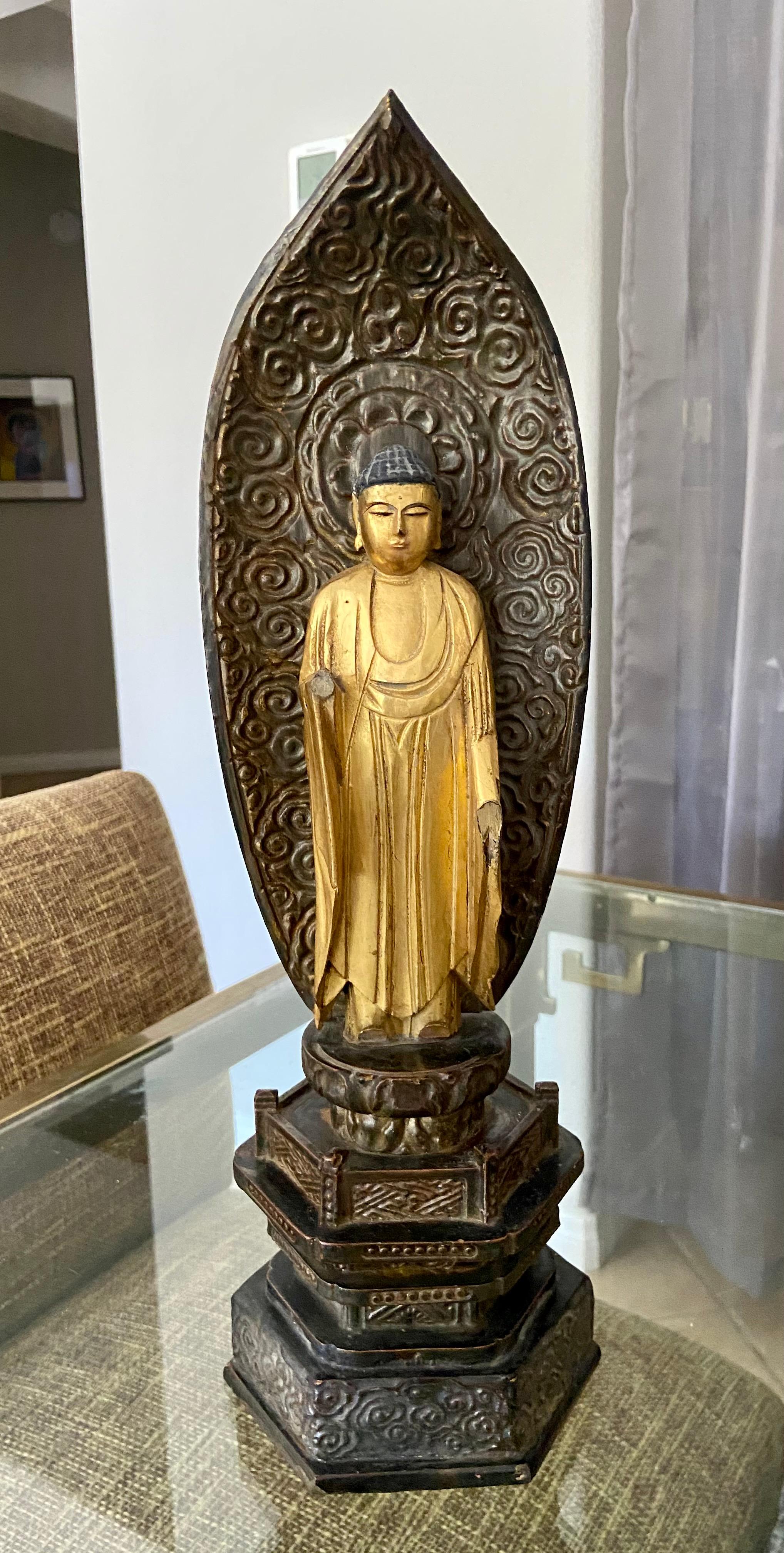 Eine lackierte und vergoldete Amida-Buddha-Gottheit aus der Edo-Zeit des 19. Die Figur steht mit den Händen in der Amida-Mudra, das Gewand ist in Falten über den Oberkörper drapiert und hängt lose über die Arme. Die Figur steht auf einem