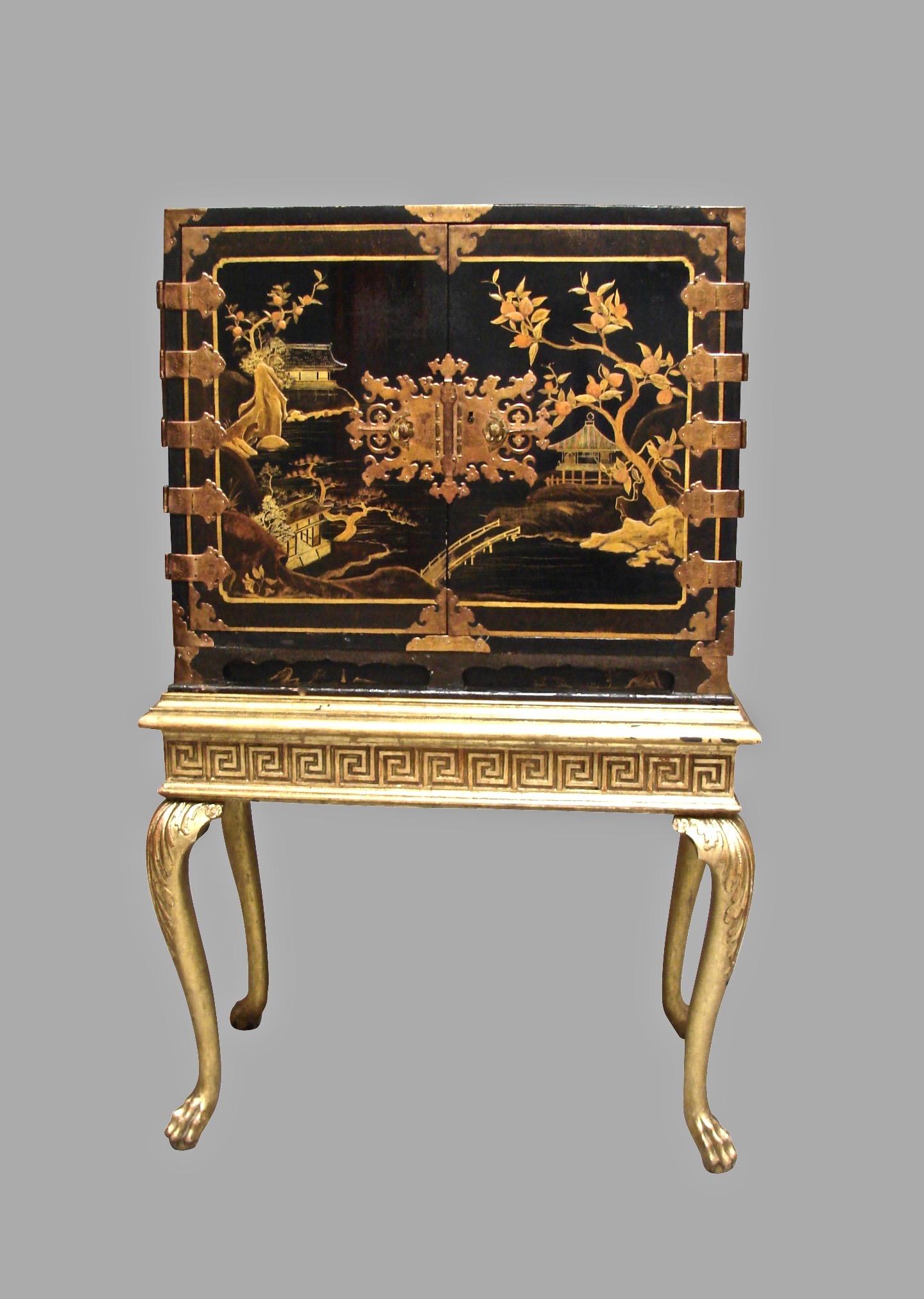 A Japanese export Edo period (1603-1868) black and gold lacquer cabinet decorated with traditional Japanese houses surrounded by trees and a bridge, the doors with elaborately engraved hinges and an ornate central lock. The interior is fitted with