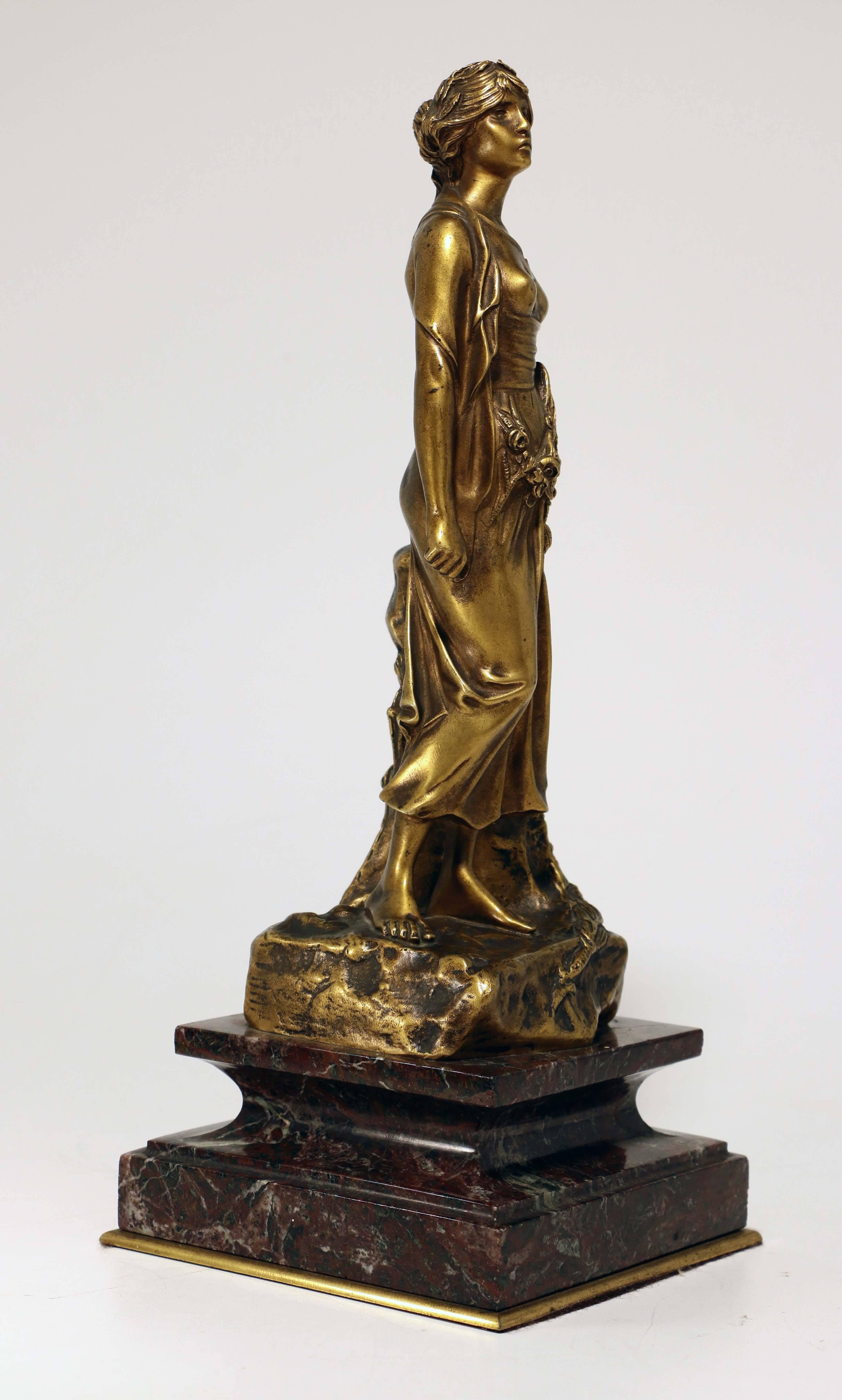 This sumptuous French bronze of an attractive young woman dates from the Belle Époque. Simply dressed in a clinging shift and with a garland of flowers at her waist, she conveys both youth and modernity, somewhat anticipating the 1920s but on this
