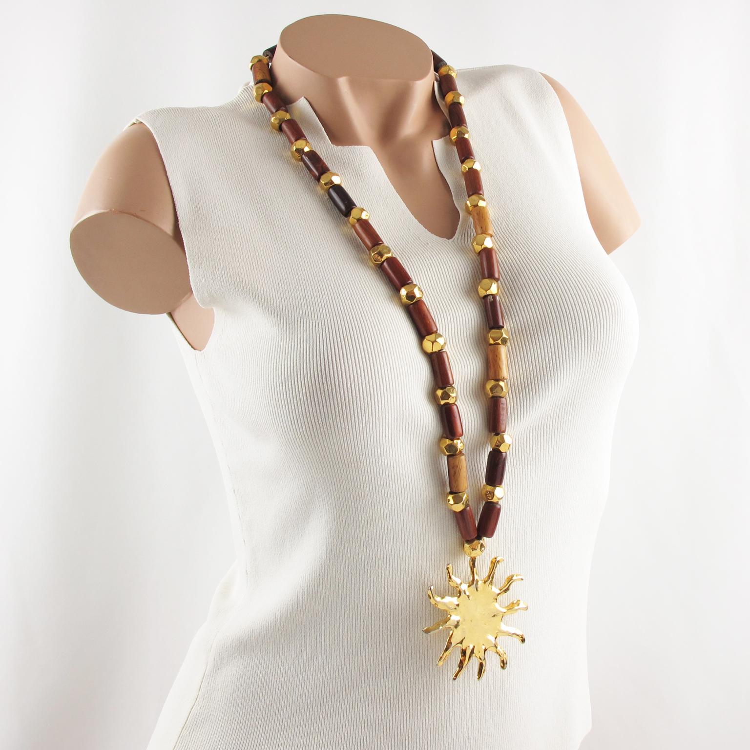 This stunning Edouard Rambaud Paris extra-long wood and metal pendant necklace features wood stick beads and gilt metal faceted beads ornate with a large shiny gilt metal medallion in a carved sun shape. There is no closing clasp, the necklace is