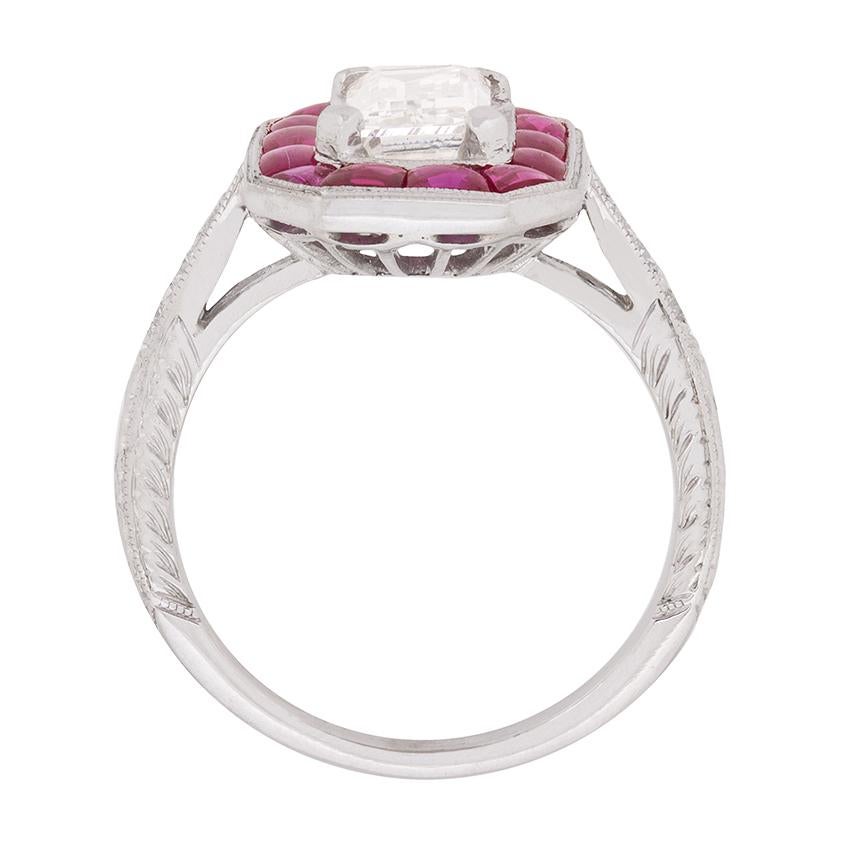 Despite its evocative Art Deco design, this beautiful and highly-detailed diamond and ruby ring originated in the 1950s. Set to centre an EDR certified, 1.10 carat, emerald cut diamond, this platinum ring is further set with a stunning halo of