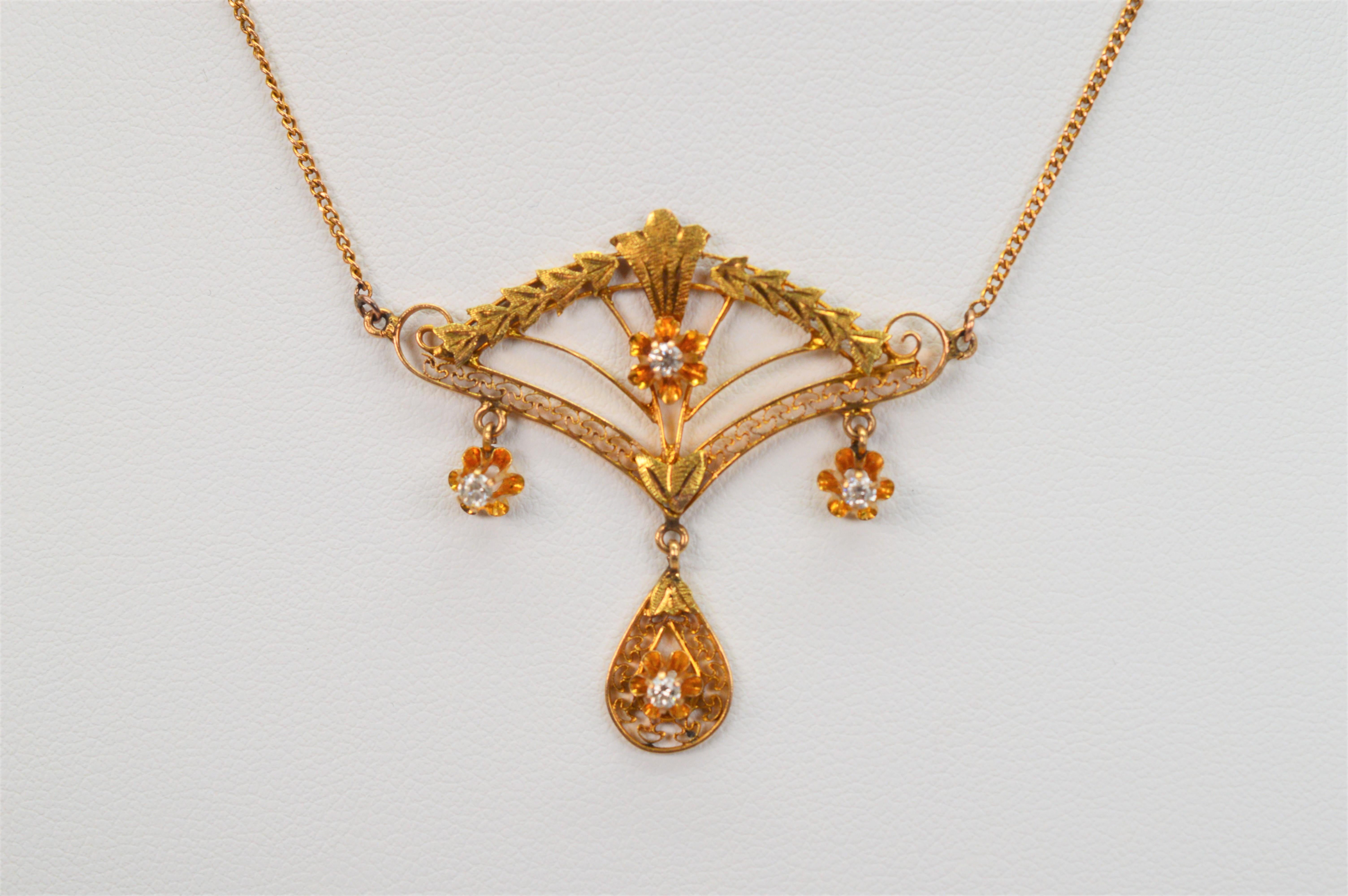 Elegant antique finery in Eduardian style is presented on this exquisite pendant necklace. An intricate and delicately appointed fan shaped filigree pendant with tear drop charm is crafted in ten karat 10K yellow gold and accented with four round