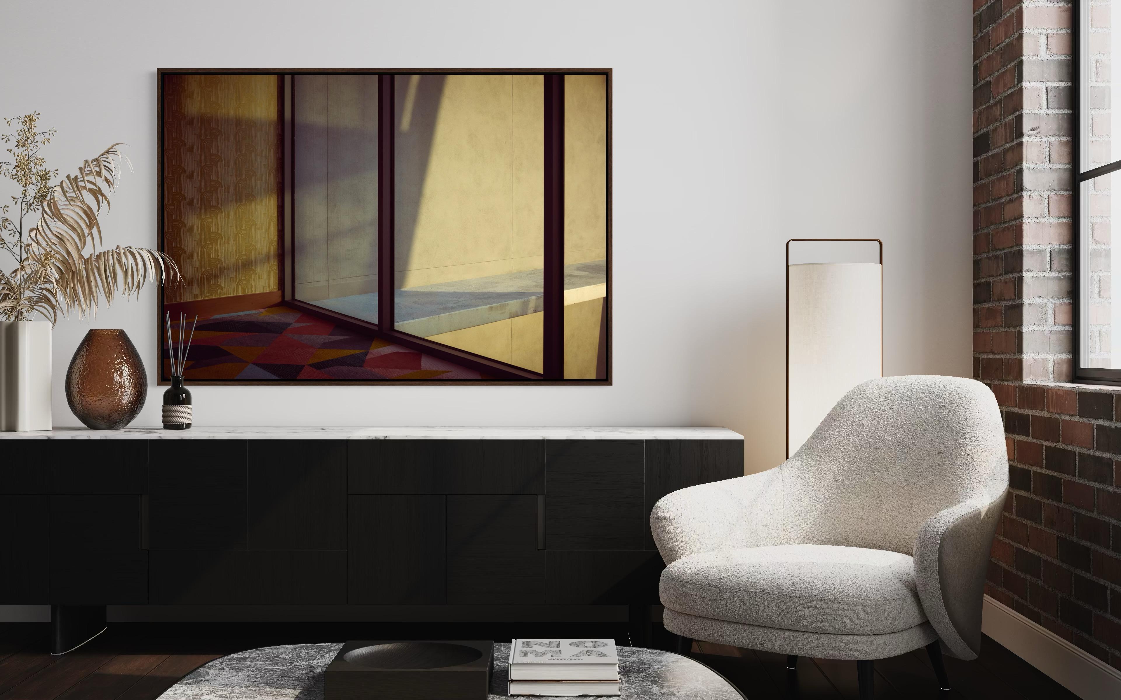 Afternoon light drafts the room with architectural restraint: bands of shadow, glass mullions, and poured concrete divide the space into calm planes, while a modernist floor in earth and rose tones introduces a subtle cadence. Nothing is hurried;