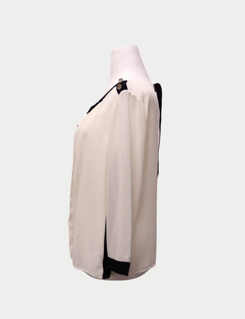 Edward Achour Paris Camicetta color crema con rifiniture nere e bottoni dorati

Sfrutta l'eleganza parigina senza tempo con questa blusa color crema di Edward Achour Paris, splendidamente rifinita con finiture nere e bottoni dorati in rilievo. La