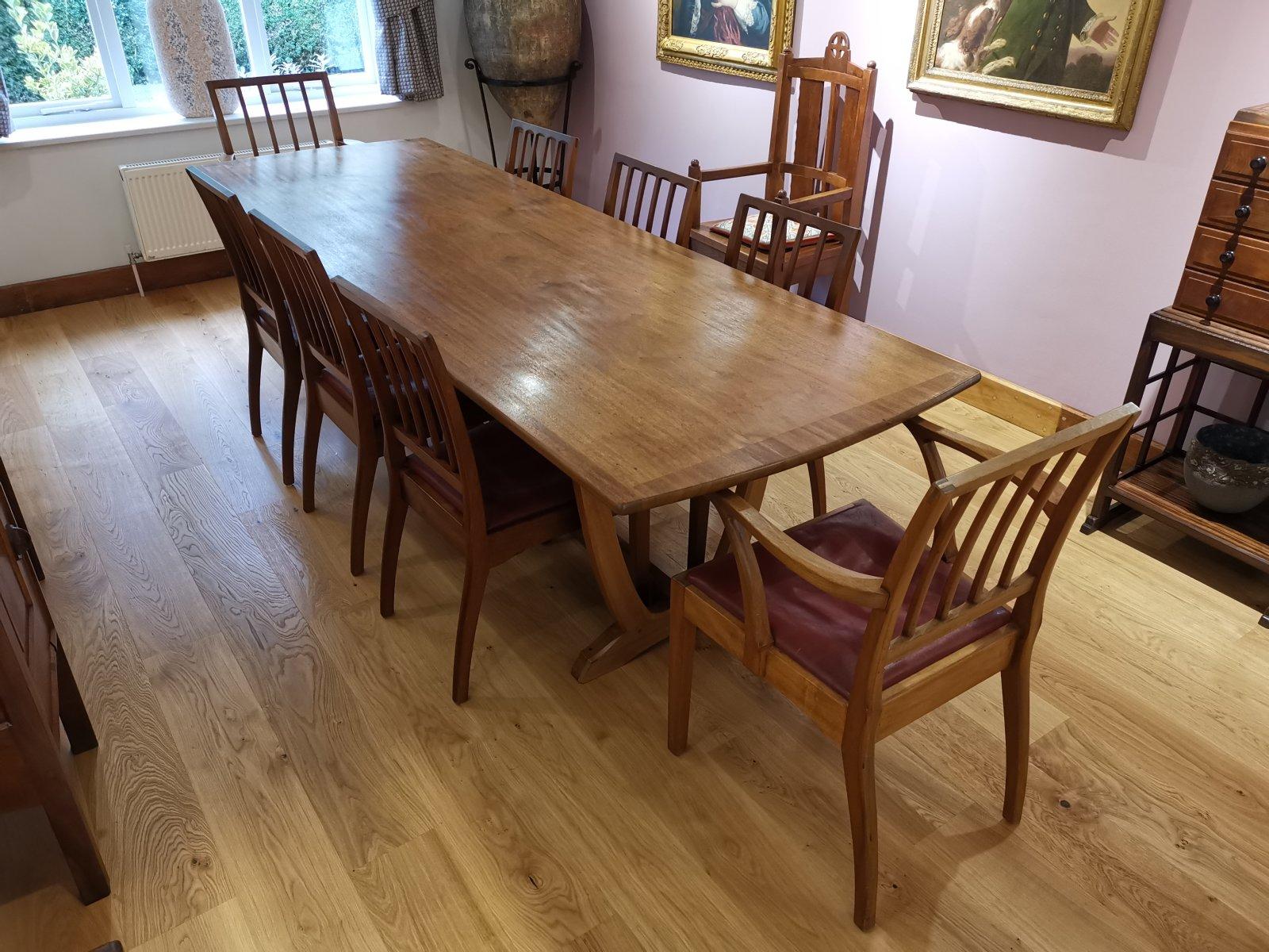 Edward Barnsley for the Rural Industries Bureau. A Walnut dining table and eight matching chairs with cross band inlay to the edges of the shaped table top and Yoke shaped end supports with through tenon construction on sculpted feet with pegged