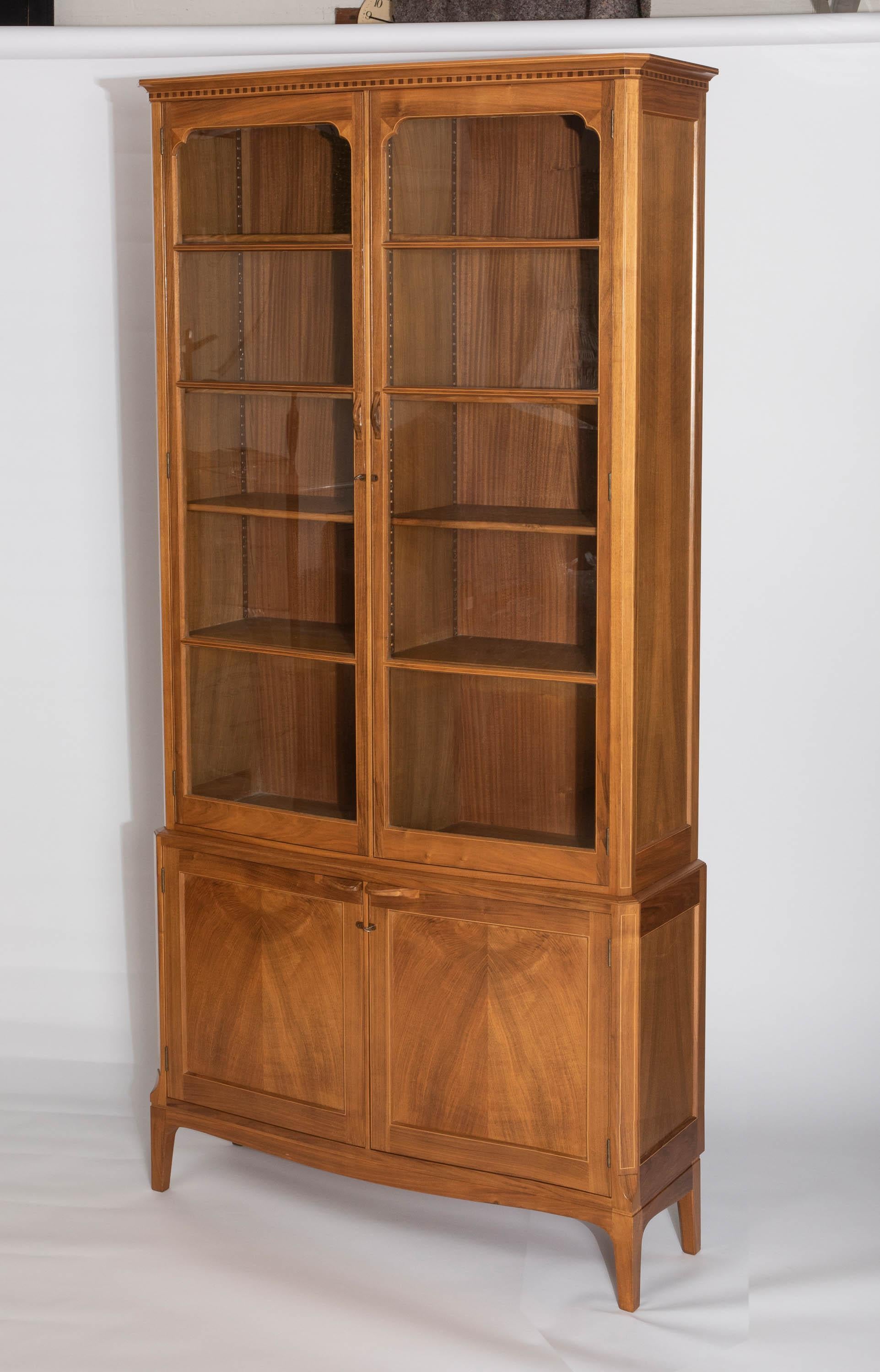 An Edward Barnsley bookcase
English walnut with sycamore stringing and ebony inlay.
Of serpentine form.
The frieze with ebony and sycamore inlay in a dentil pattern.
With serpentine glazed doors above a pair of cupboards.
D shaped handles.