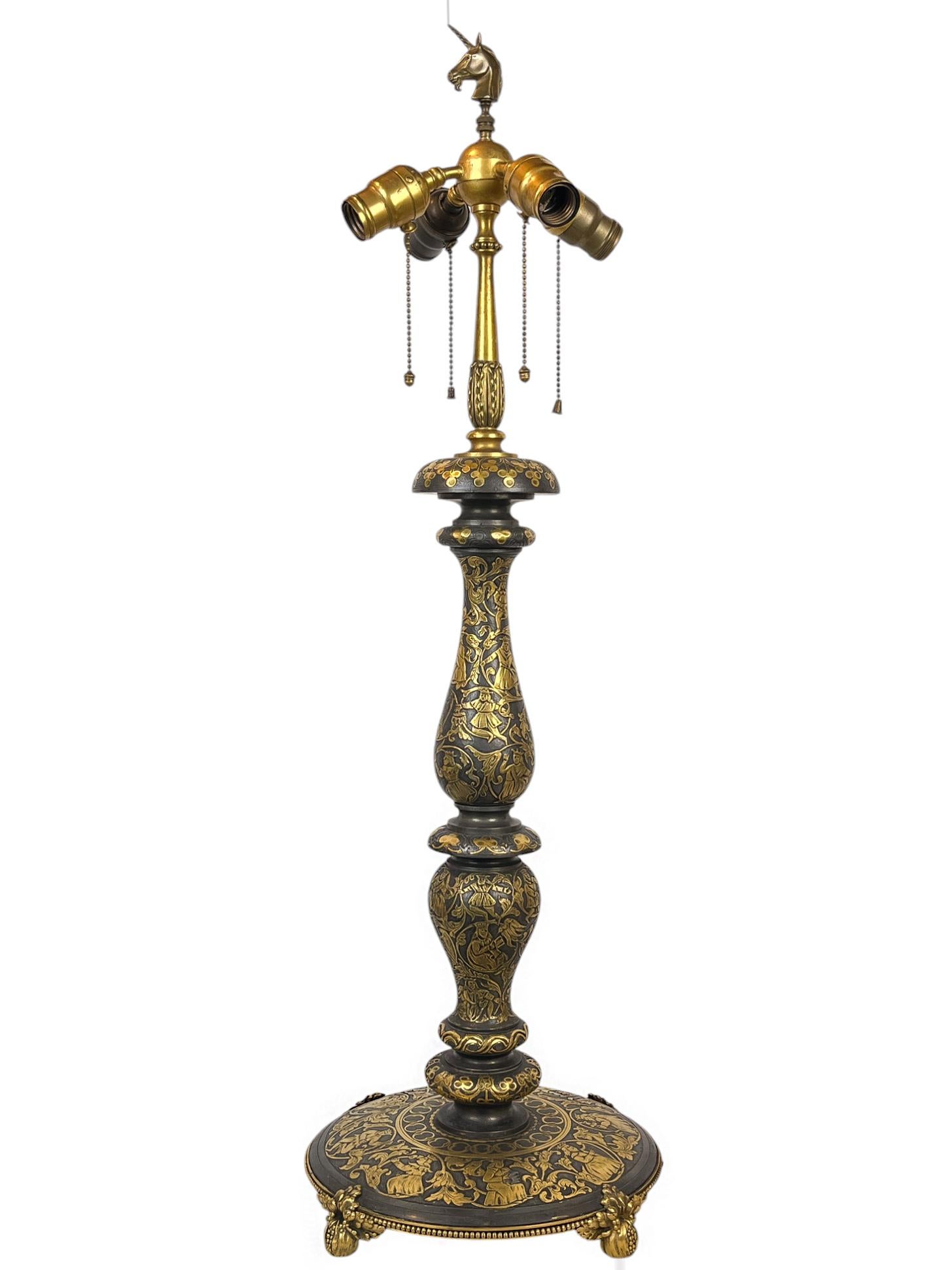 A silvered renaissance revival style table lamp with mythical accents. Gilded designs resembling the drawings of illuminated manuscripts with figures, scroll forms, acanthus leaves and trefoils. Topped by a unicorn finial, the entire composition