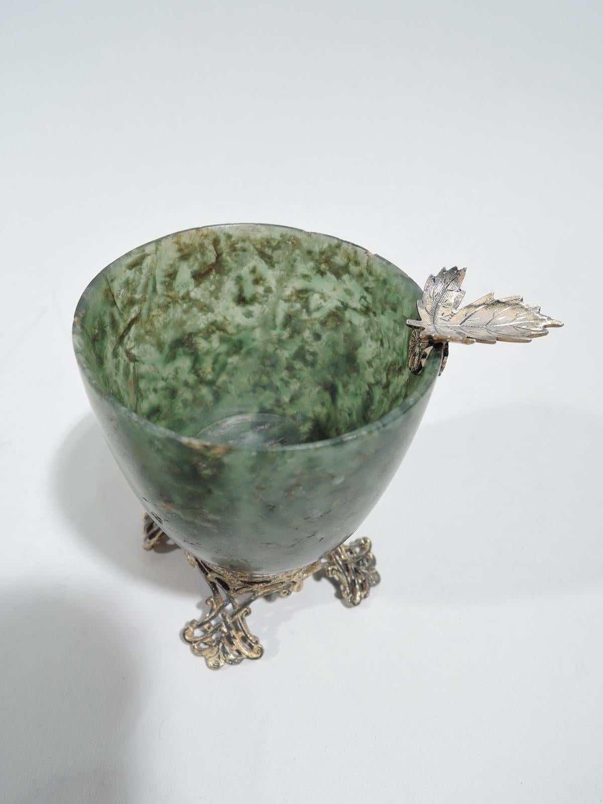 Chinese-style bowl, ca 1920. Mottled green hardstone urn on silver gilt fretwork base with 4 splayed supports. A pretty ornament that works as an ashtray with silver gilt leaf cradle mounted to rim. Marked “Edward I Farmer / Sterling”. 

Overall