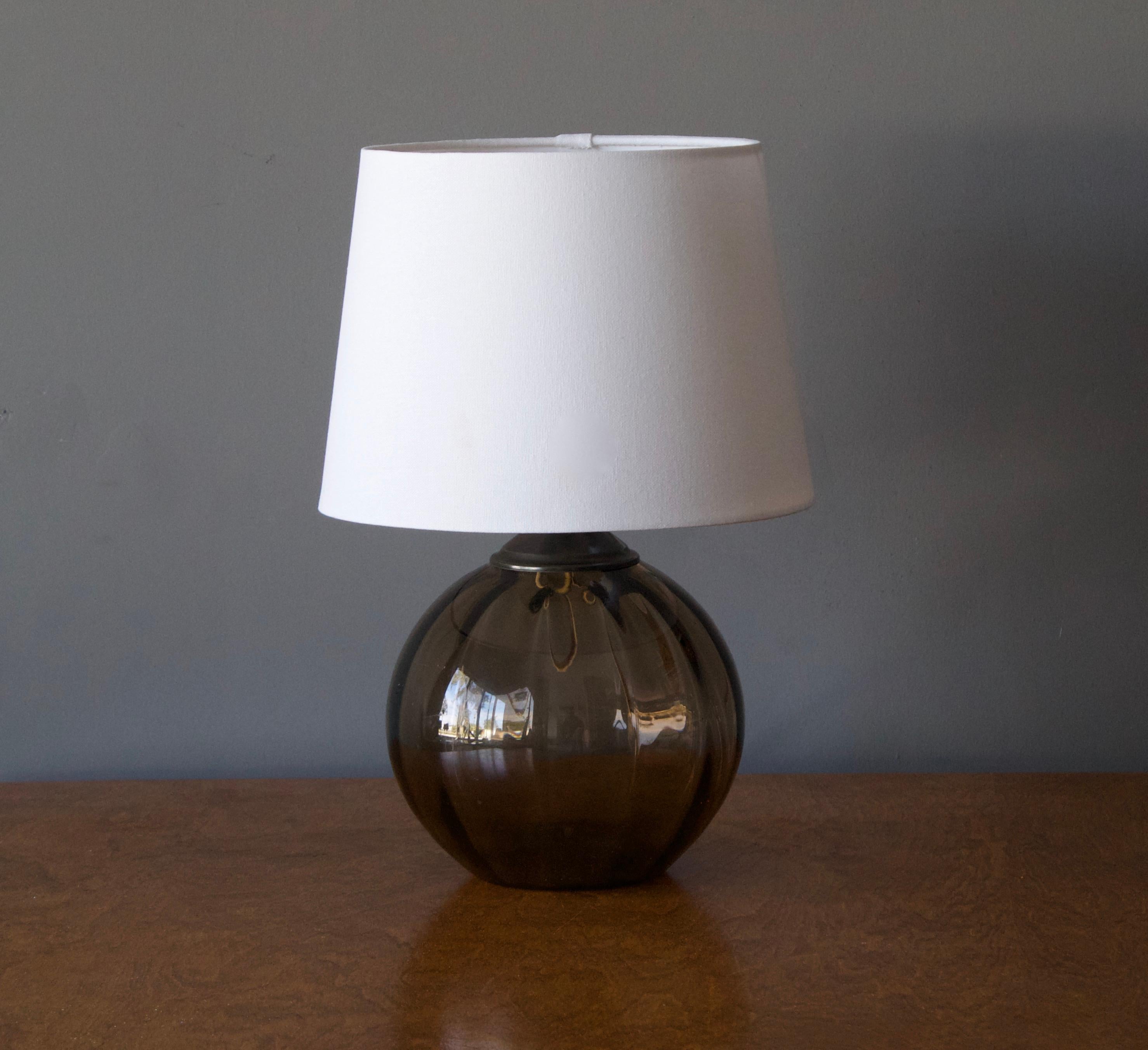 A modernist table lamp, design attributed to Edward Hald. Production attributed to Orrefors, c. 1930s. Blown smoked glass, patinated brass, porcelein socket. 

Stated dimensions exclude lampshade. Height includes socket. Sold without lampshade.
